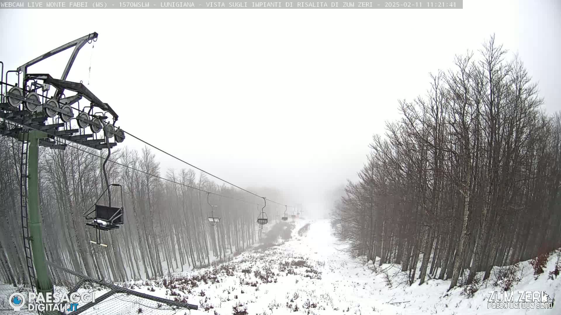 A snow-covered ski lift ascends a hill through a hazy, snowy forest.
