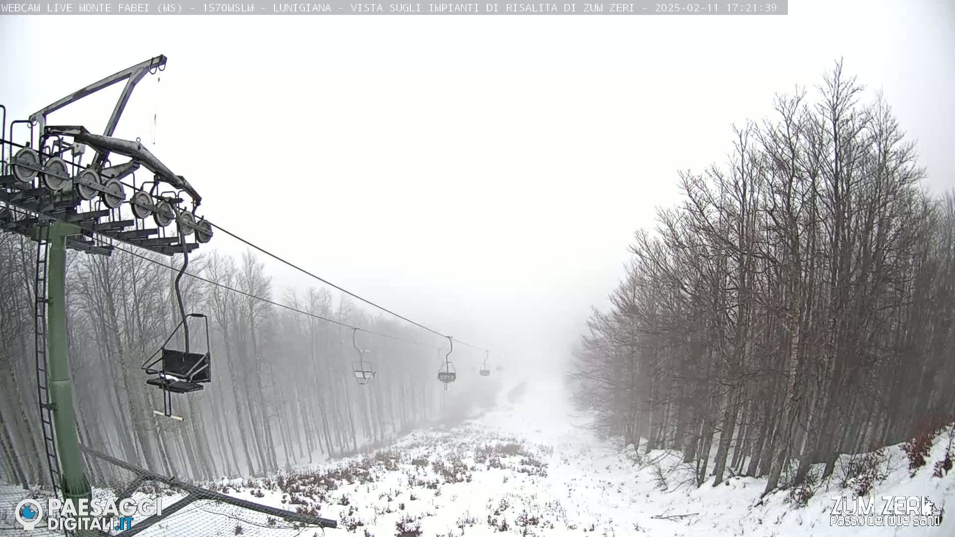 A snow-covered ski lift with several empty chairs extends into a foggy, snowy forest.