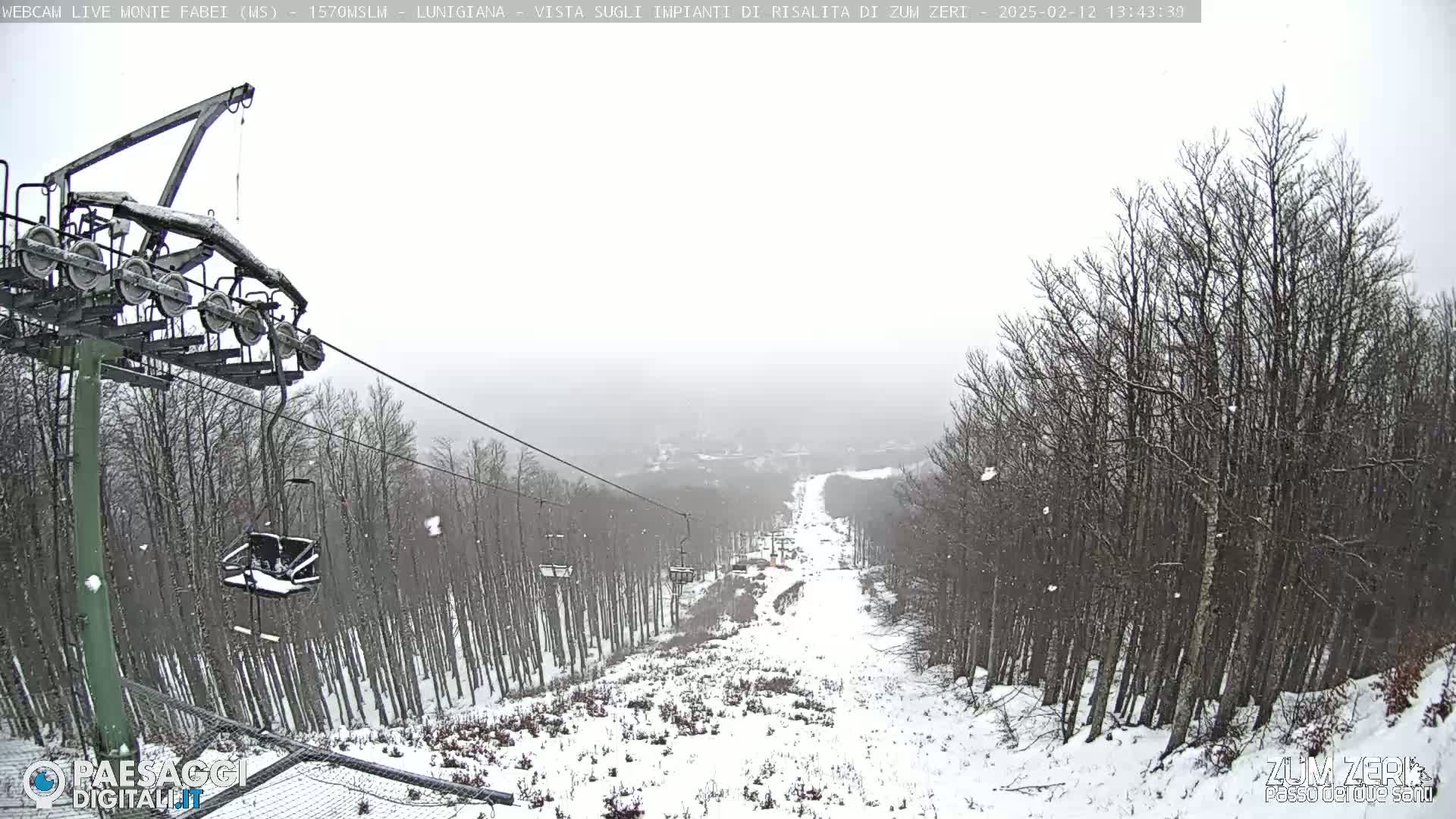 A snow-covered ski slope with a chairlift and bare trees is visible during a light snowfall.