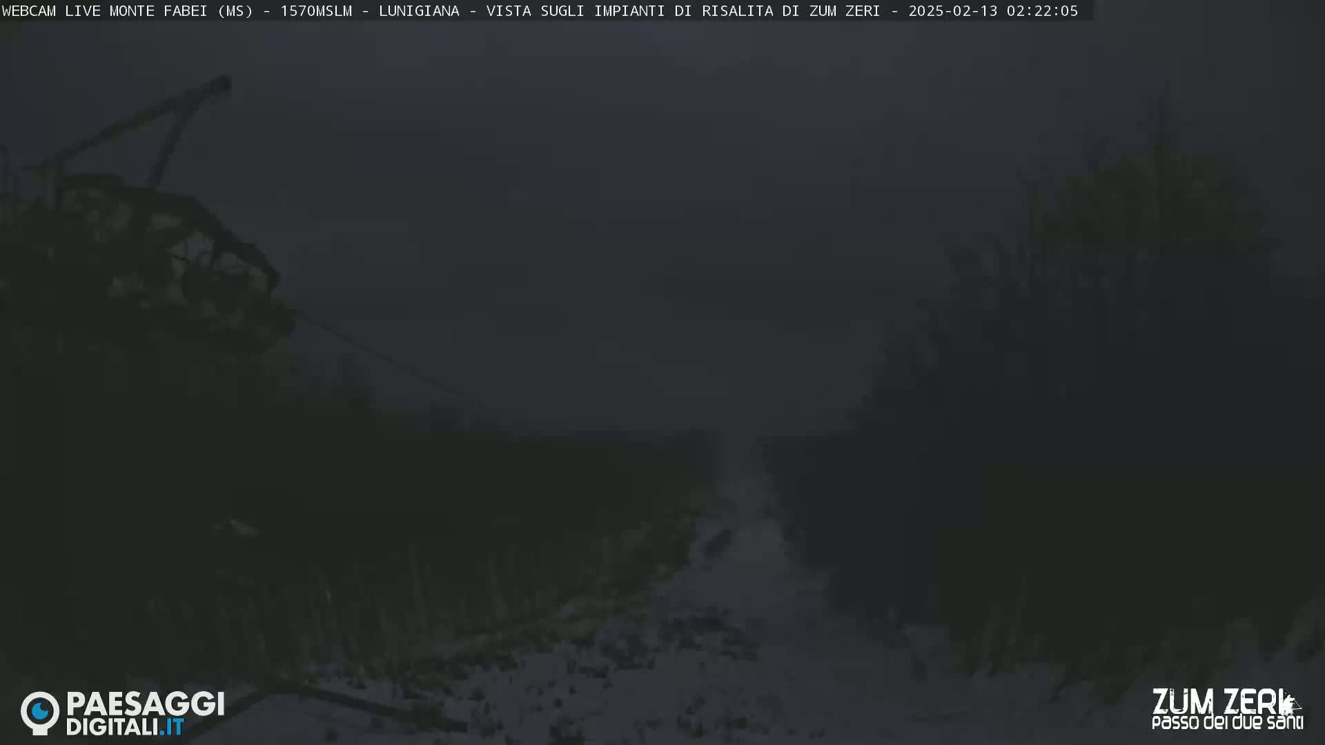 A dark, snowy scene at night shows a portion of a ski lift against a dimly lit landscape.