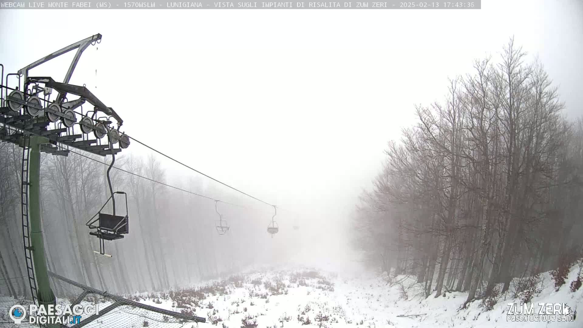 A chairlift ascends through a snowy, foggy forest.