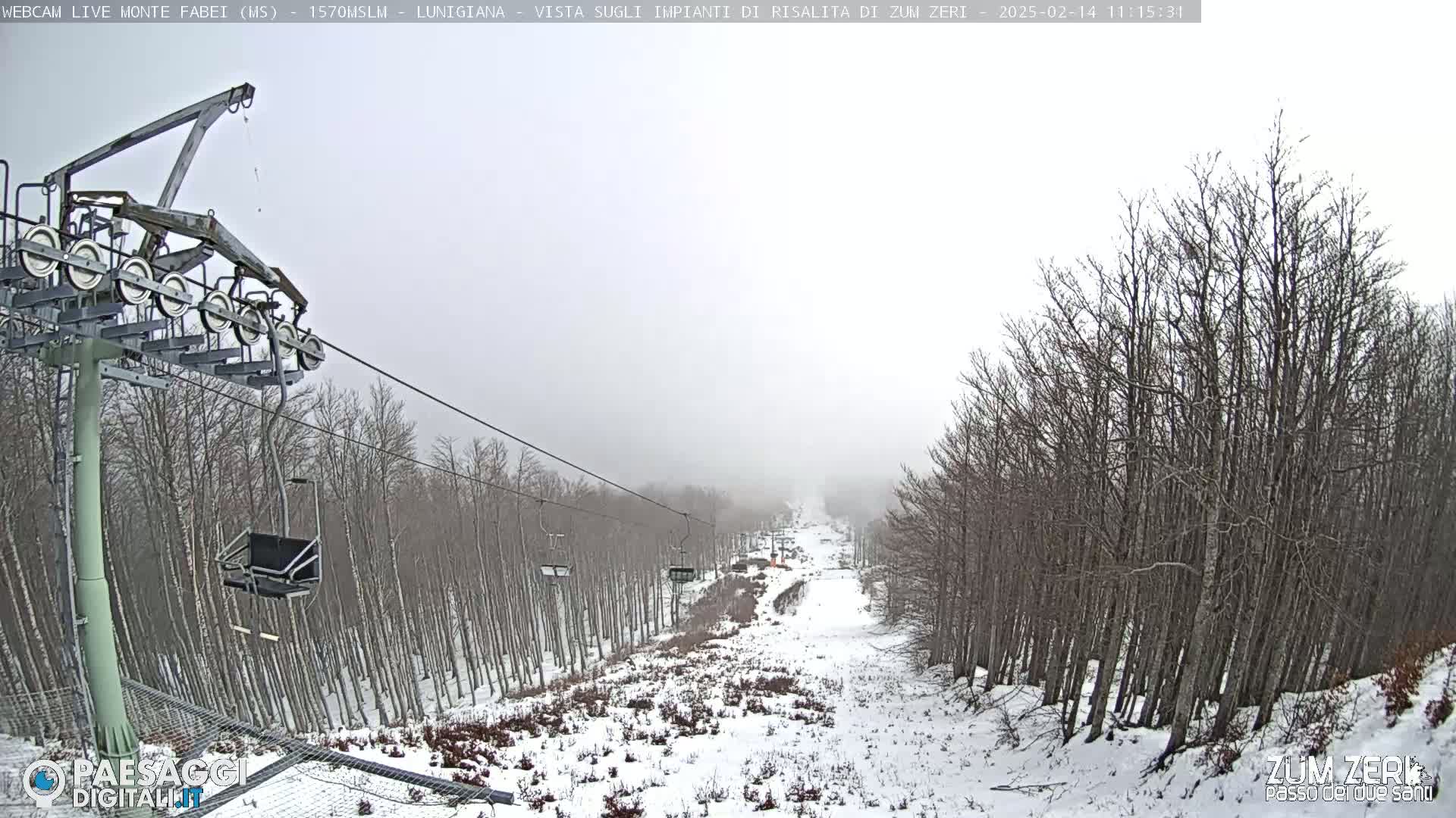 A snow-covered ski slope with a chairlift and bare trees in foggy conditions.