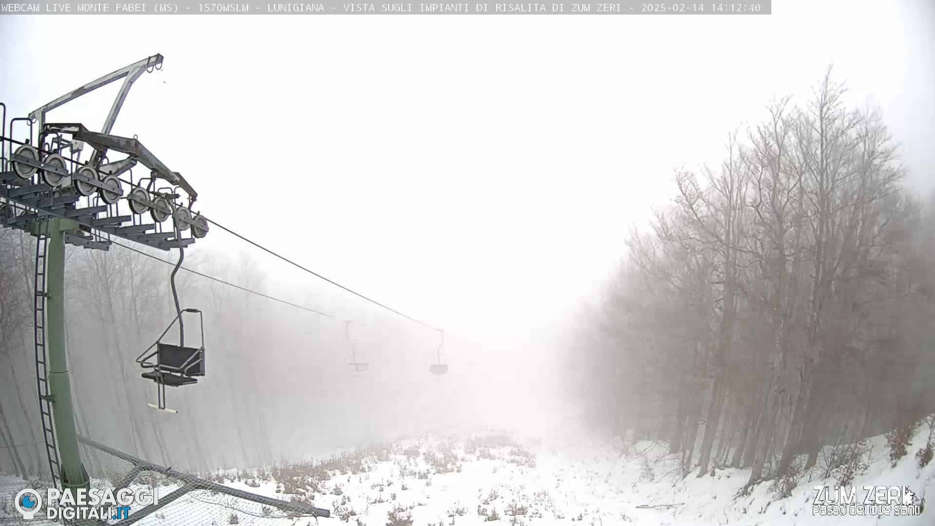 A chairlift ascends a snow-covered hill shrouded in dense fog, with bare trees lining the sides.
