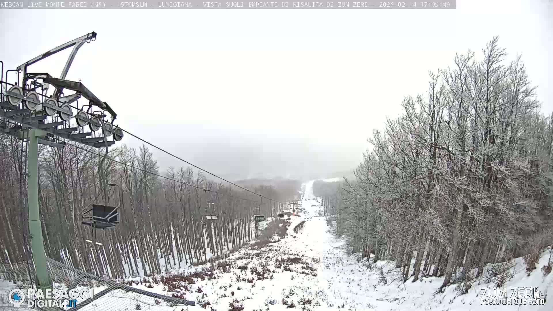 A snow-covered ski slope with a chairlift and sparsely-treed landscape is visible during a light snowfall.