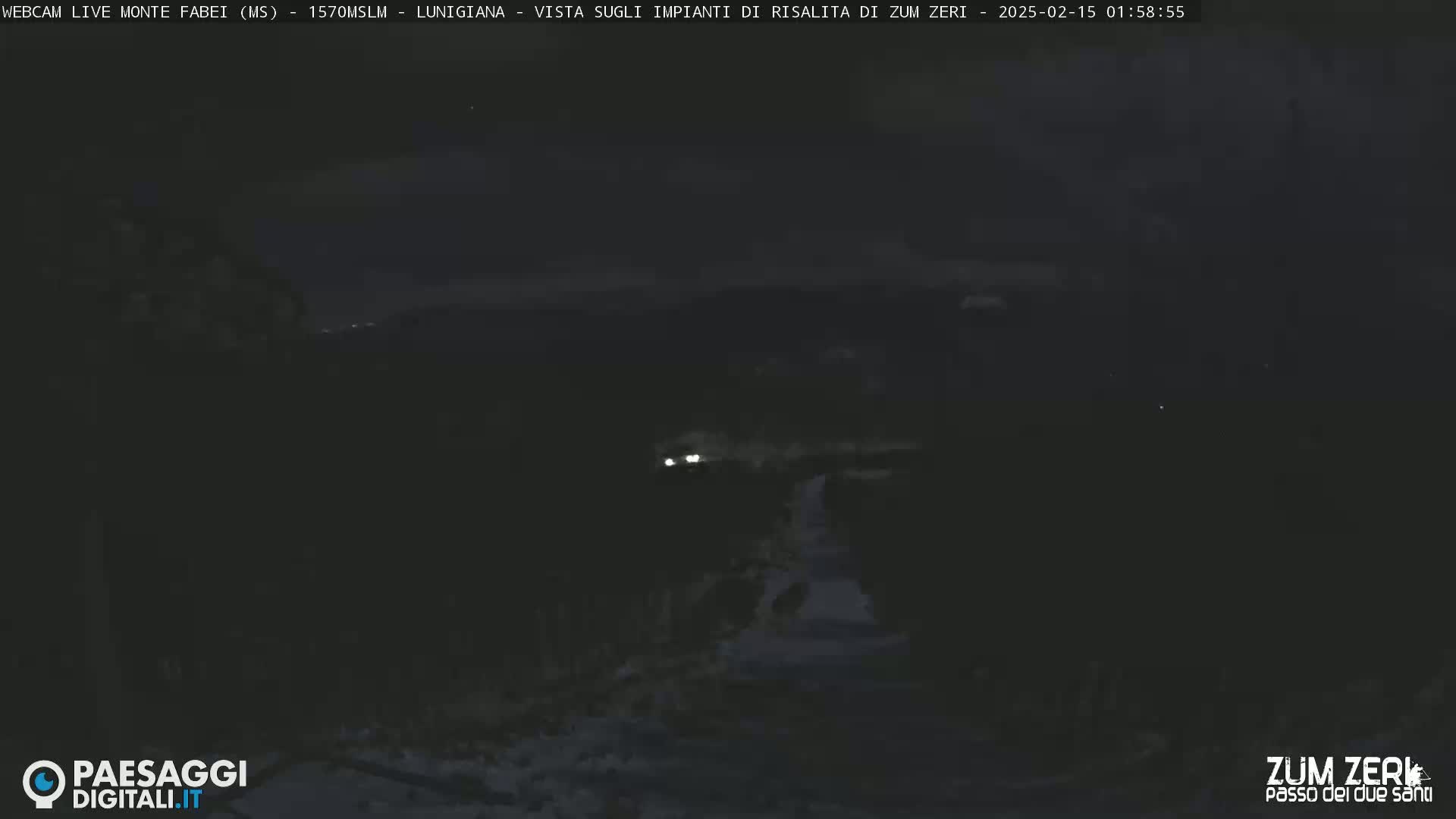 A nighttime, dark view of a road leading toward faintly visible headlights in the distance.