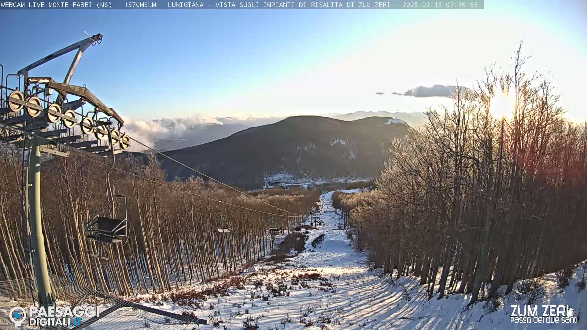 A snowy ski slope descends through a forest of leafless trees, bathed in the bright light of a sunrise.