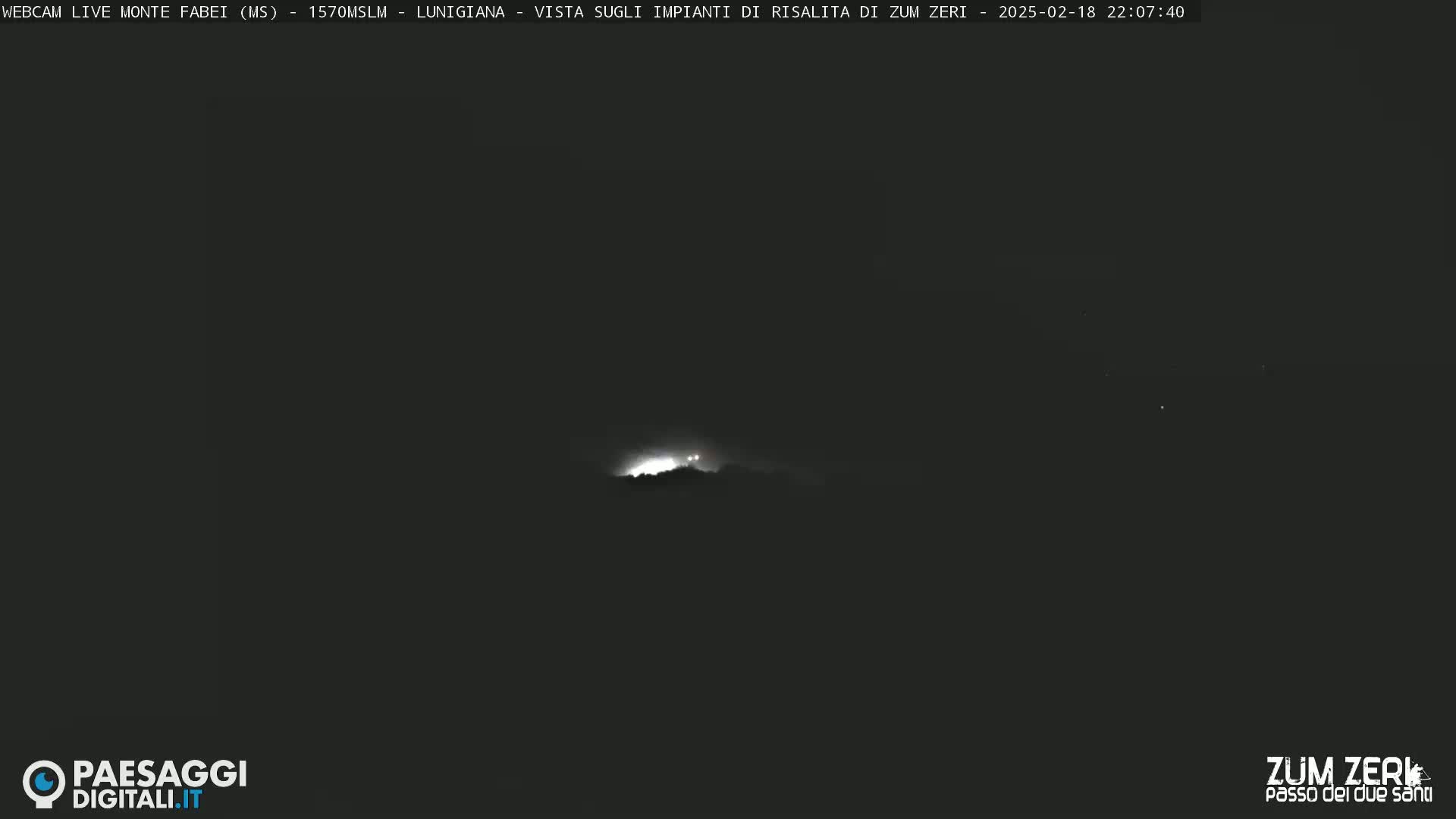 A nighttime long shot shows faint lights atop a hill or mountain under a dark, possibly cloudy sky.