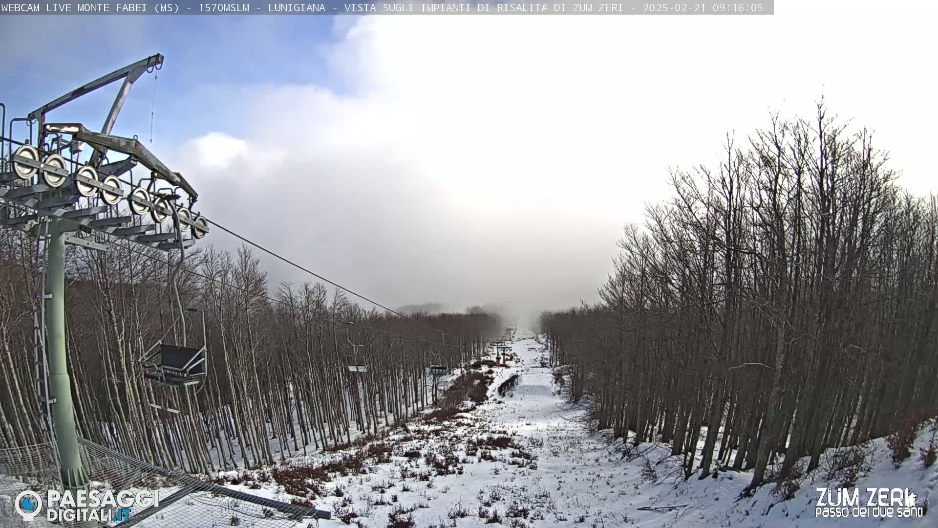 A snowy ski slope is visible from a chairlift, with bare trees lining the sides and a hazy sky overhead.