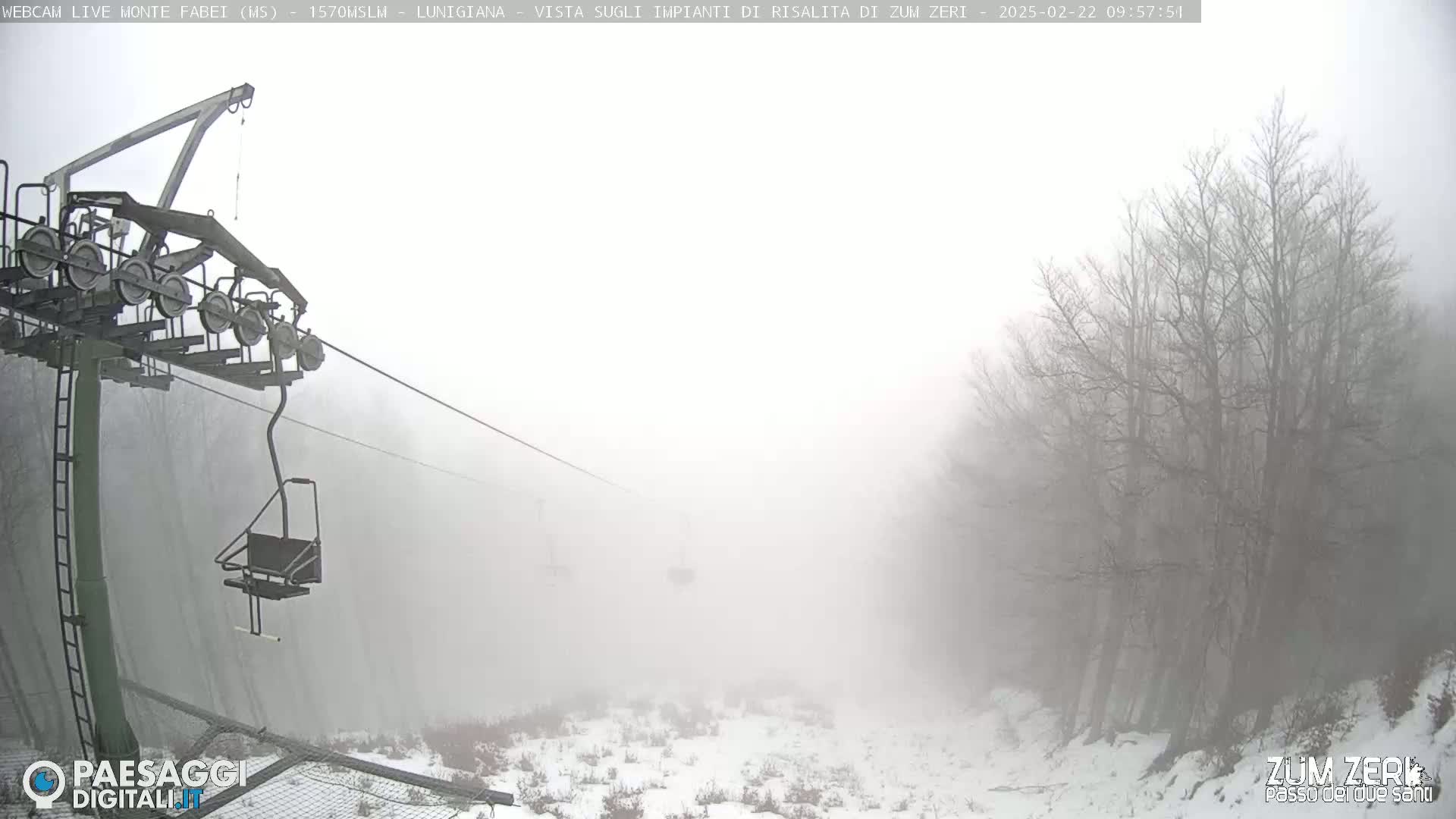 A chairlift ascends into a dense fog over a snow-covered landscape of leafless trees.