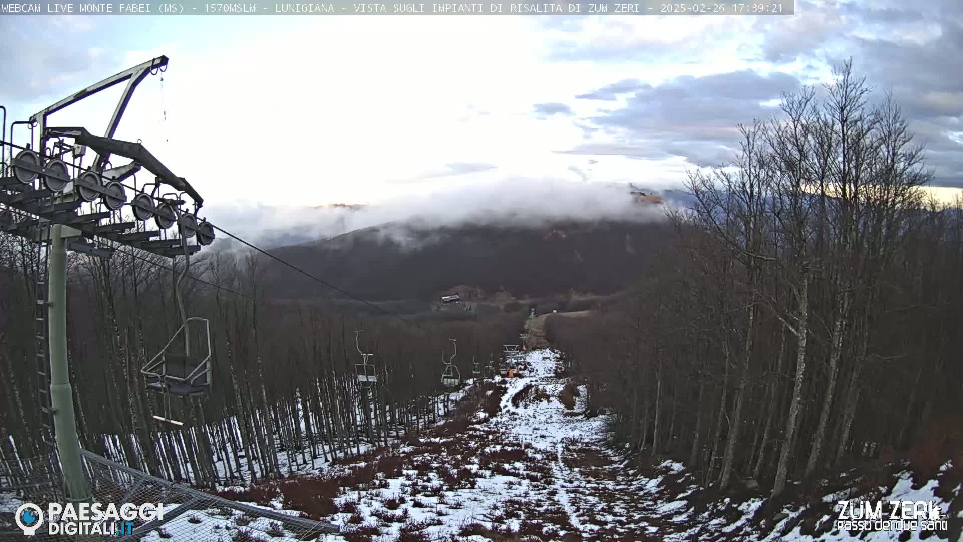 A chairlift ascends a snow-dusted mountainside under a cloudy sky.