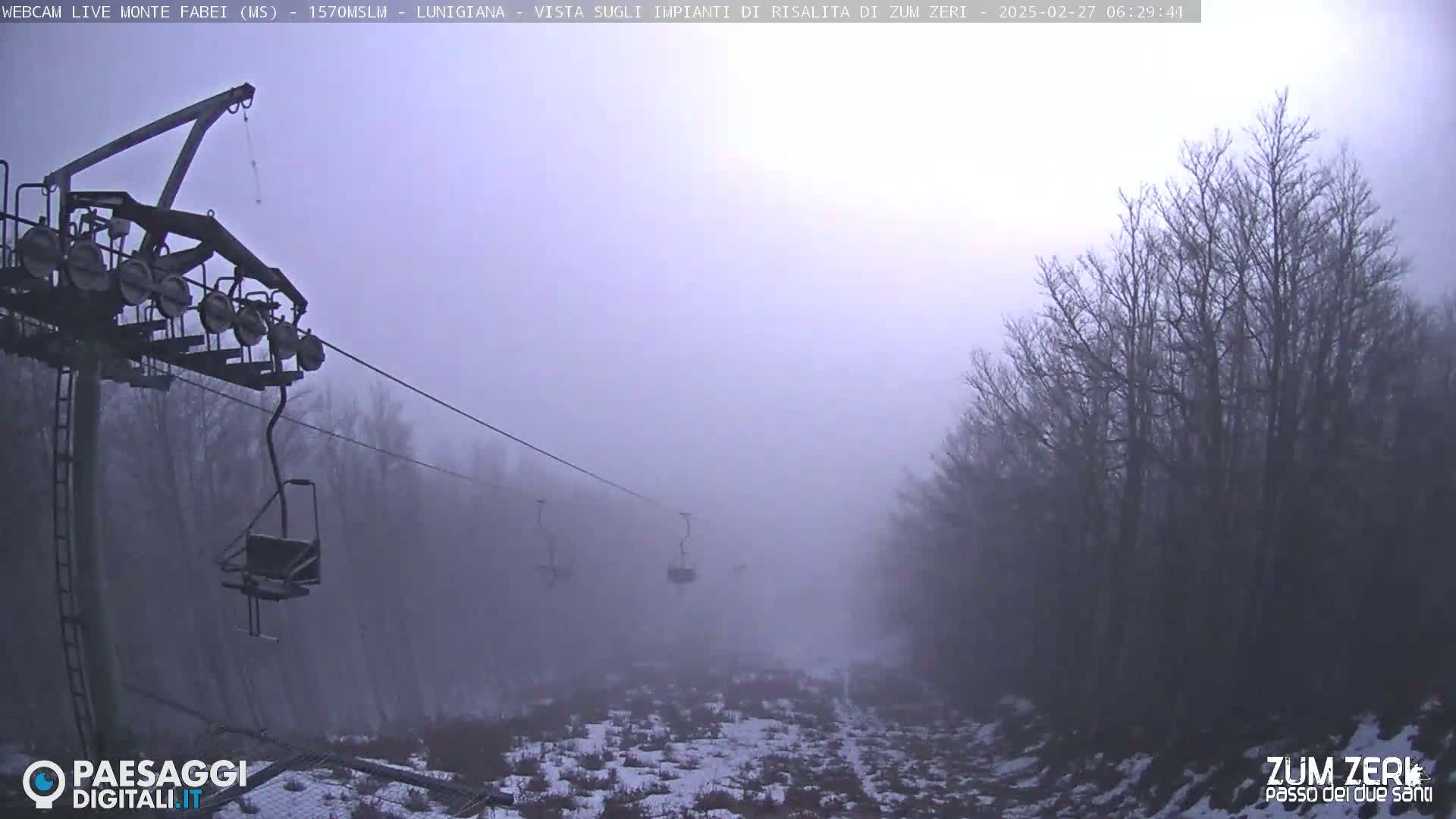 A foggy landscape shows a ski lift and sparsely snow-covered ground with bare trees.