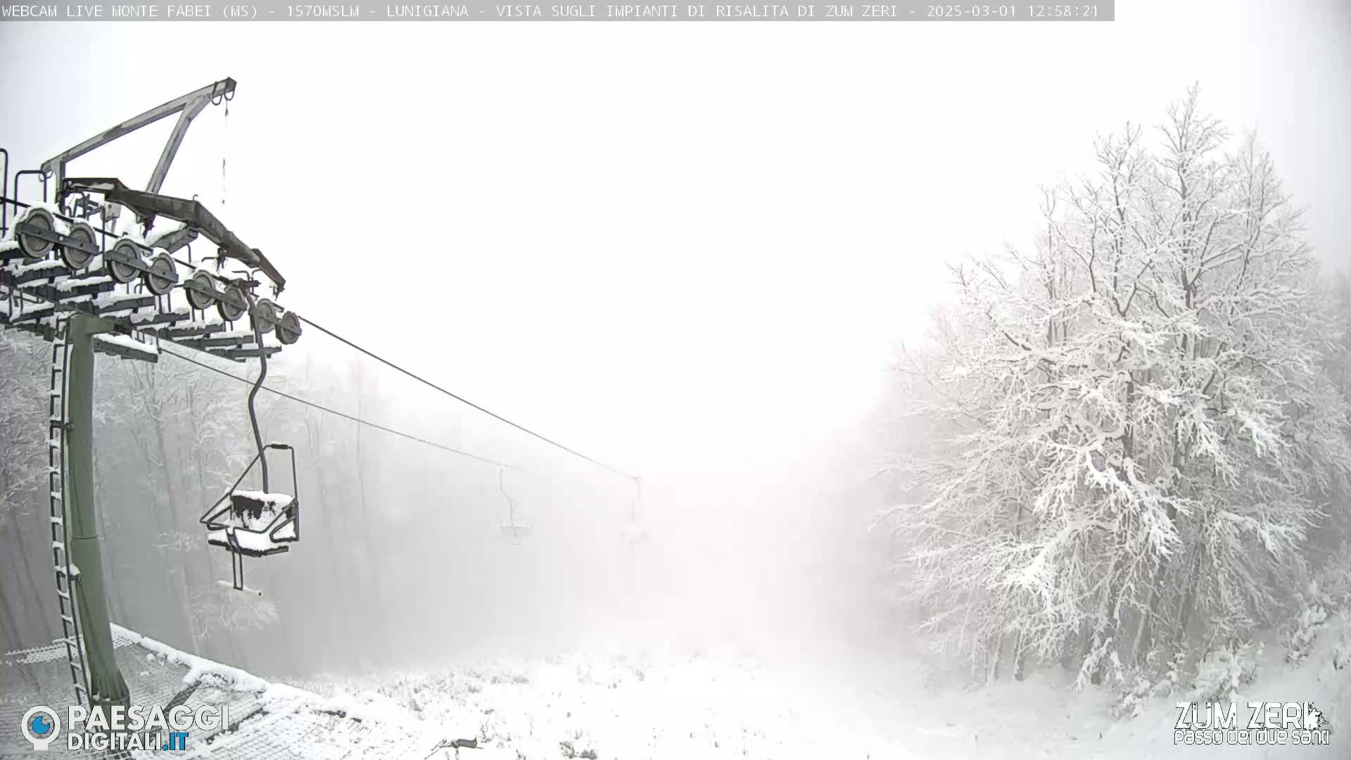 A snow-covered ski lift chair hangs from a cable in a foggy, snowy landscape.