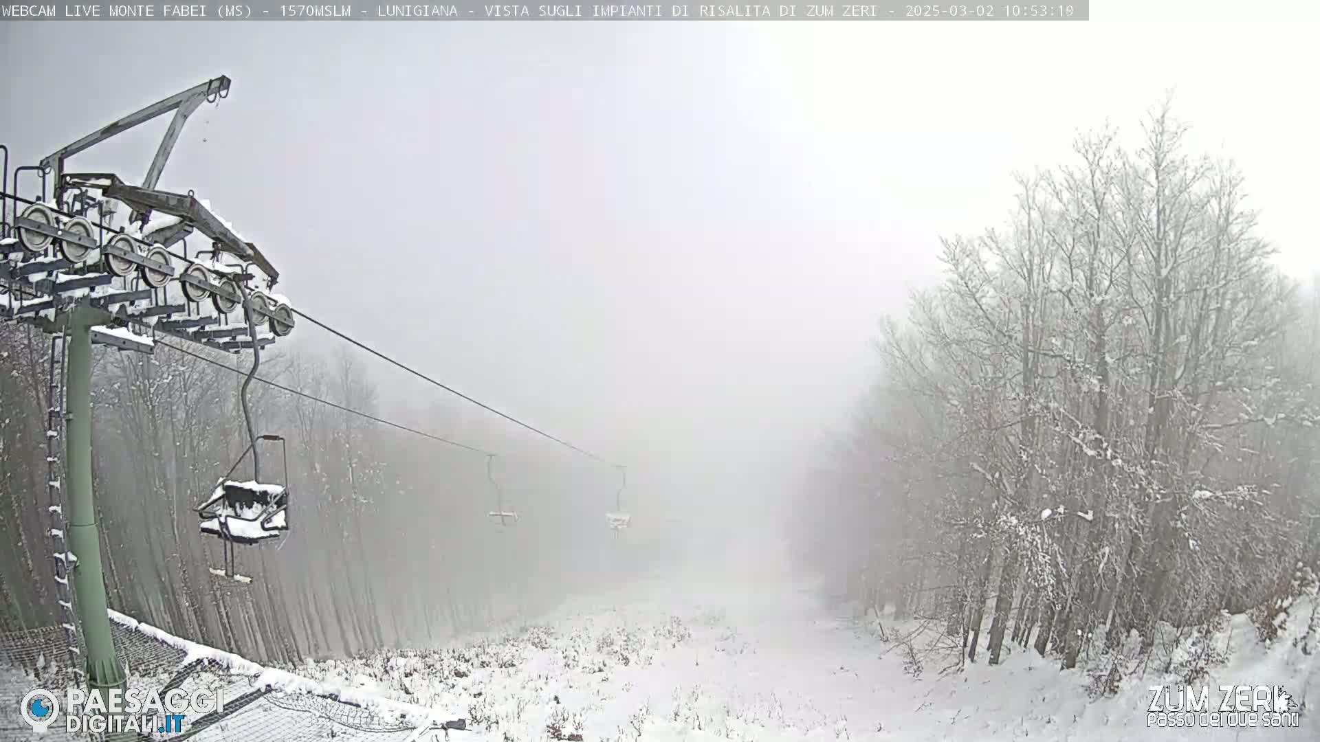 A snow-covered ski lift ascends through a foggy, snowy landscape.