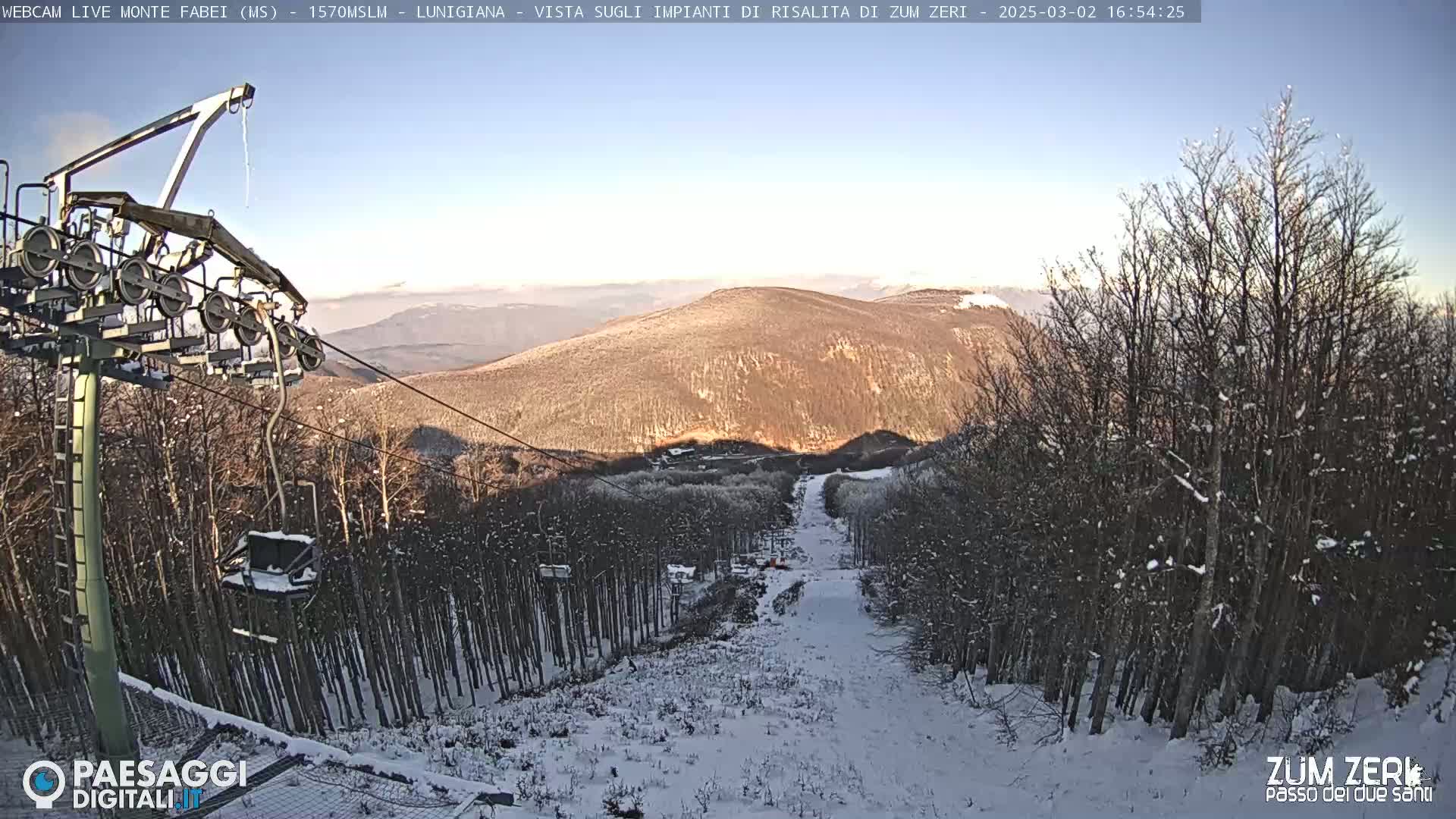 A chairlift ascends a snowy mountain slope, surrounded by snow-covered trees under a clear, bright sky.