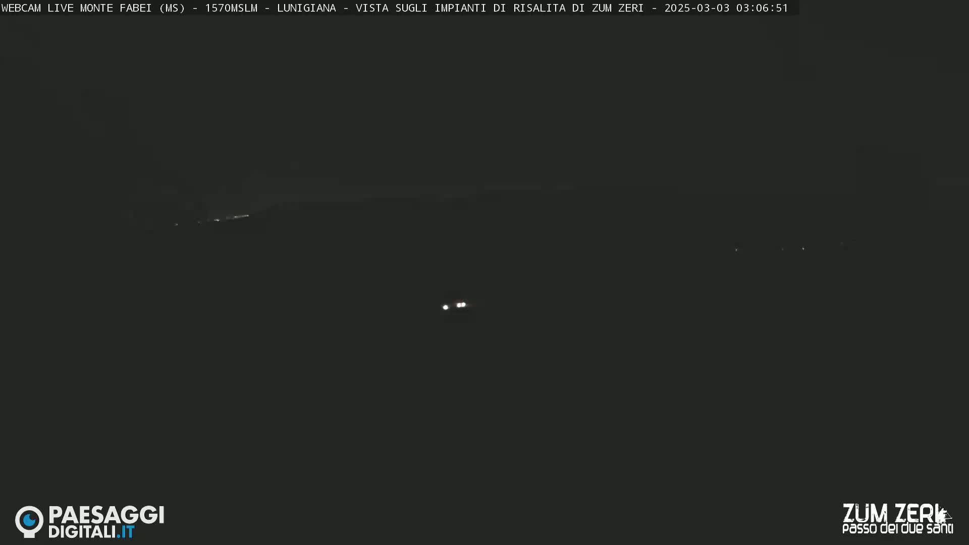 A dark, nighttime scene shows a few faint lights in the distance.