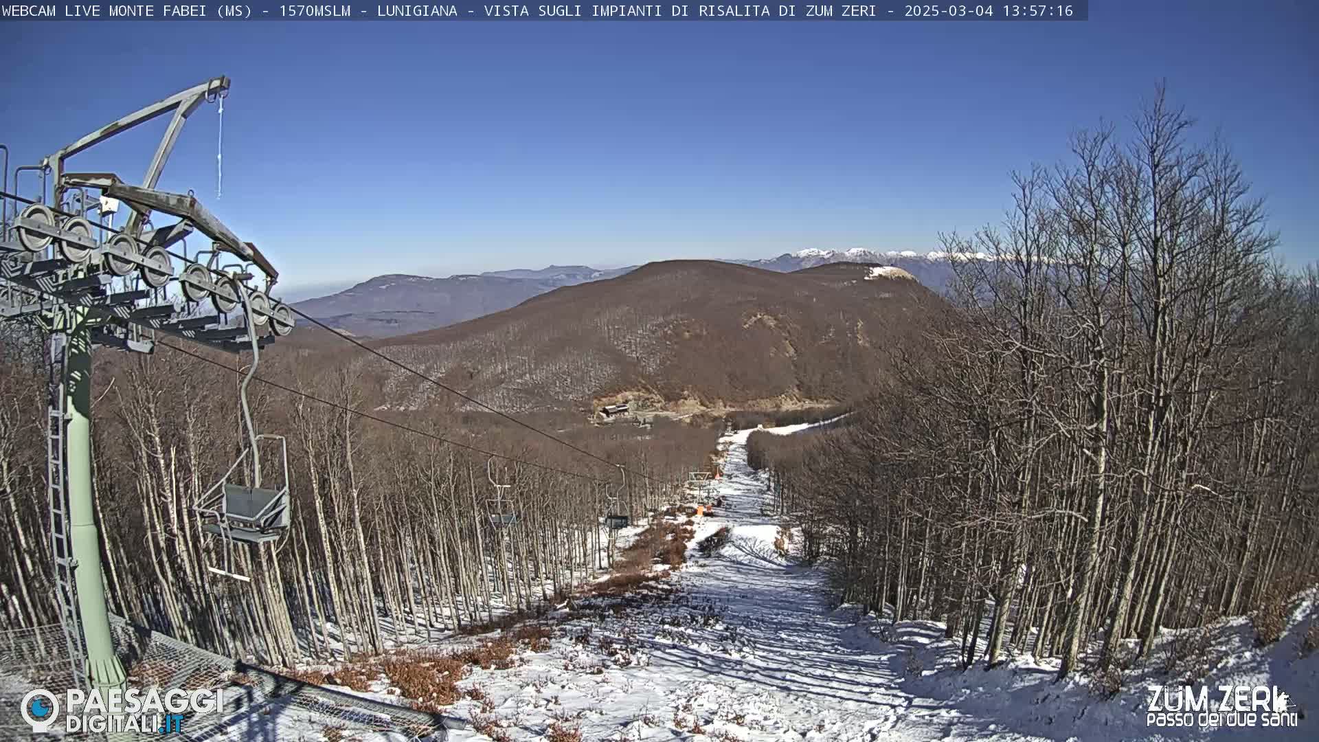 A ski lift descends a snowy mountainside under a clear blue sky.
