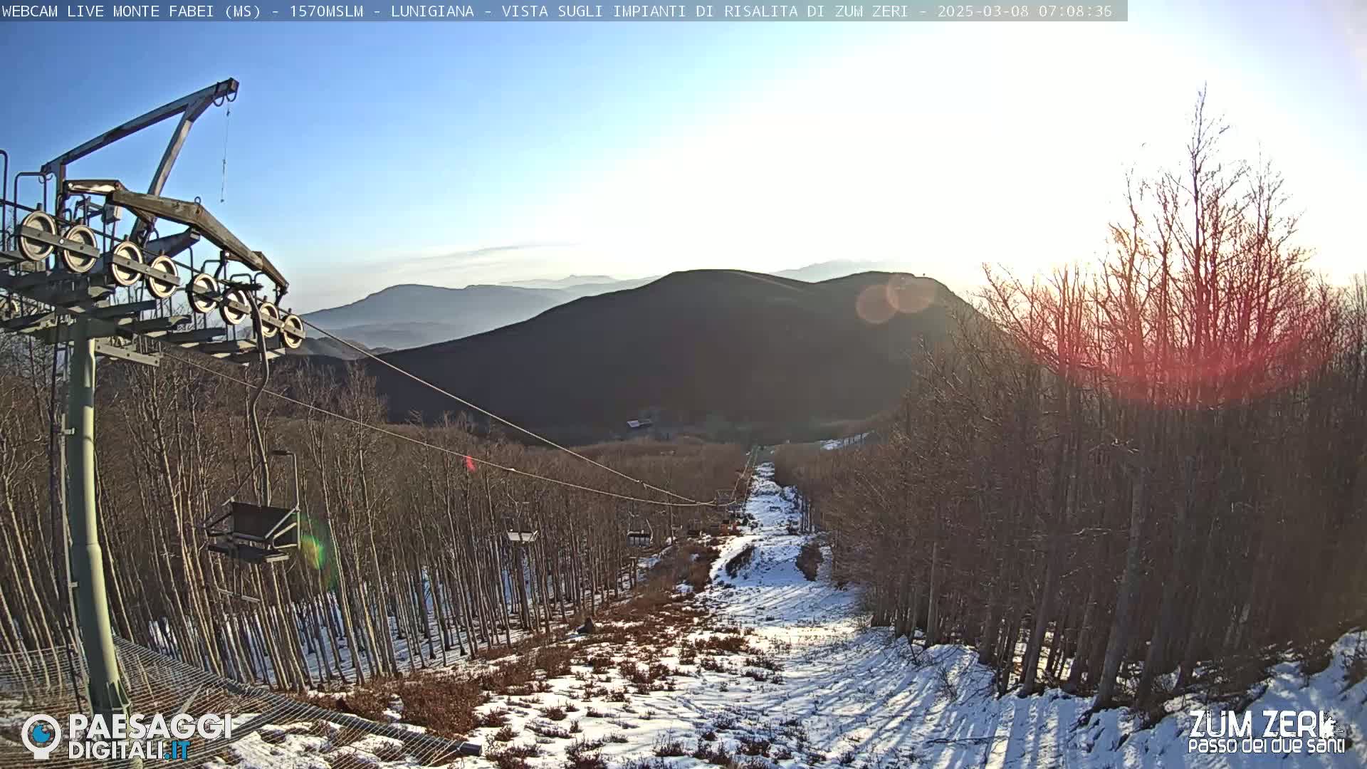 A chairlift ascends a snow-dusted mountainside under a mostly sunny sky.