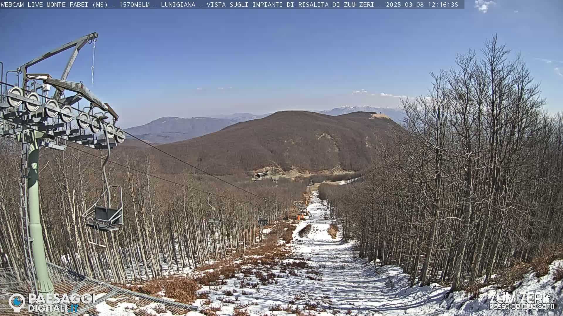 A chairlift ascends a mountainside ski slope with patchy snow under a clear blue sky.