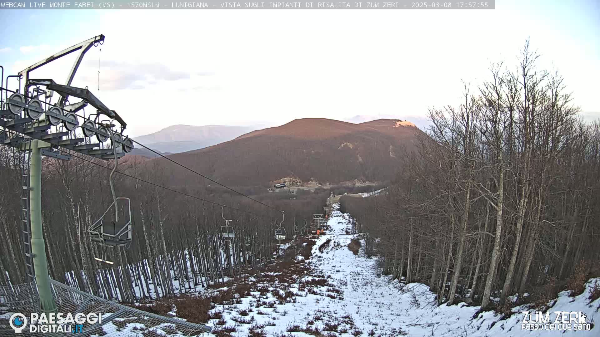 A ski lift ascends a snow-dusted mountainside under a clear, twilight sky.