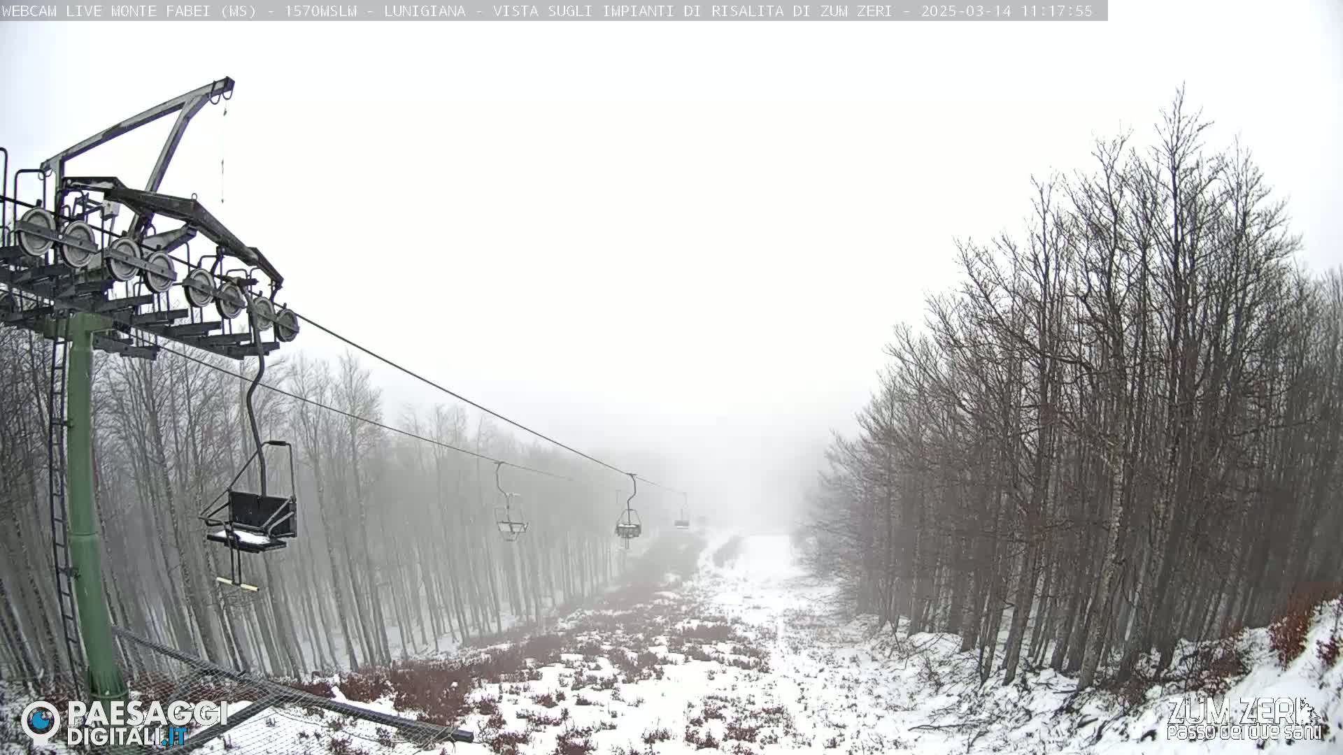 A snow-covered ski lift ascends through a foggy forest.