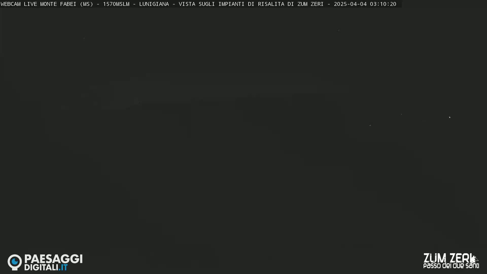 A dark, nighttime image shows a mostly featureless black landscape with a few faint lights visible in the distance.