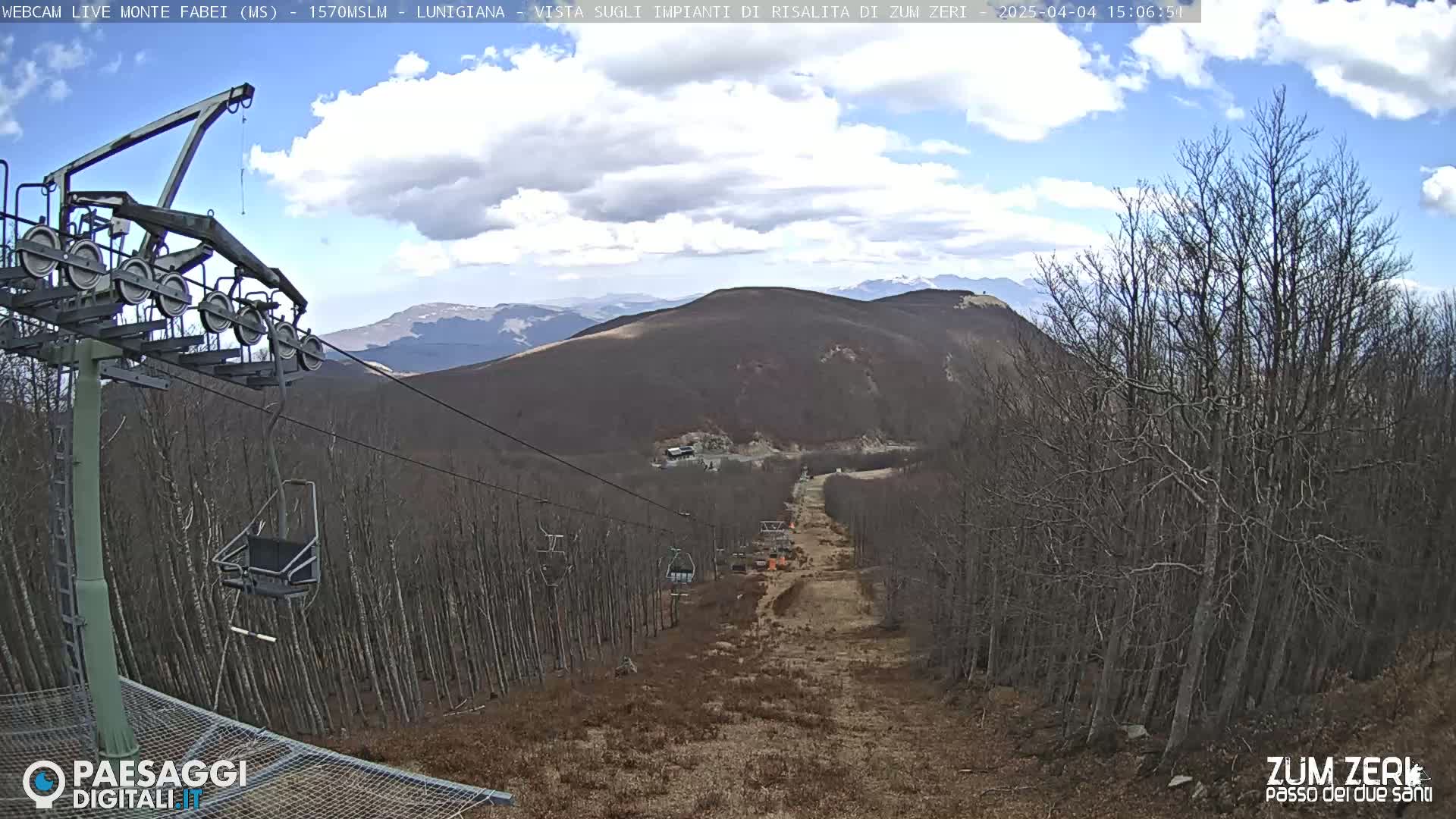 A chairlift ascends a sparsely vegetated mountainside under a partly cloudy sky.