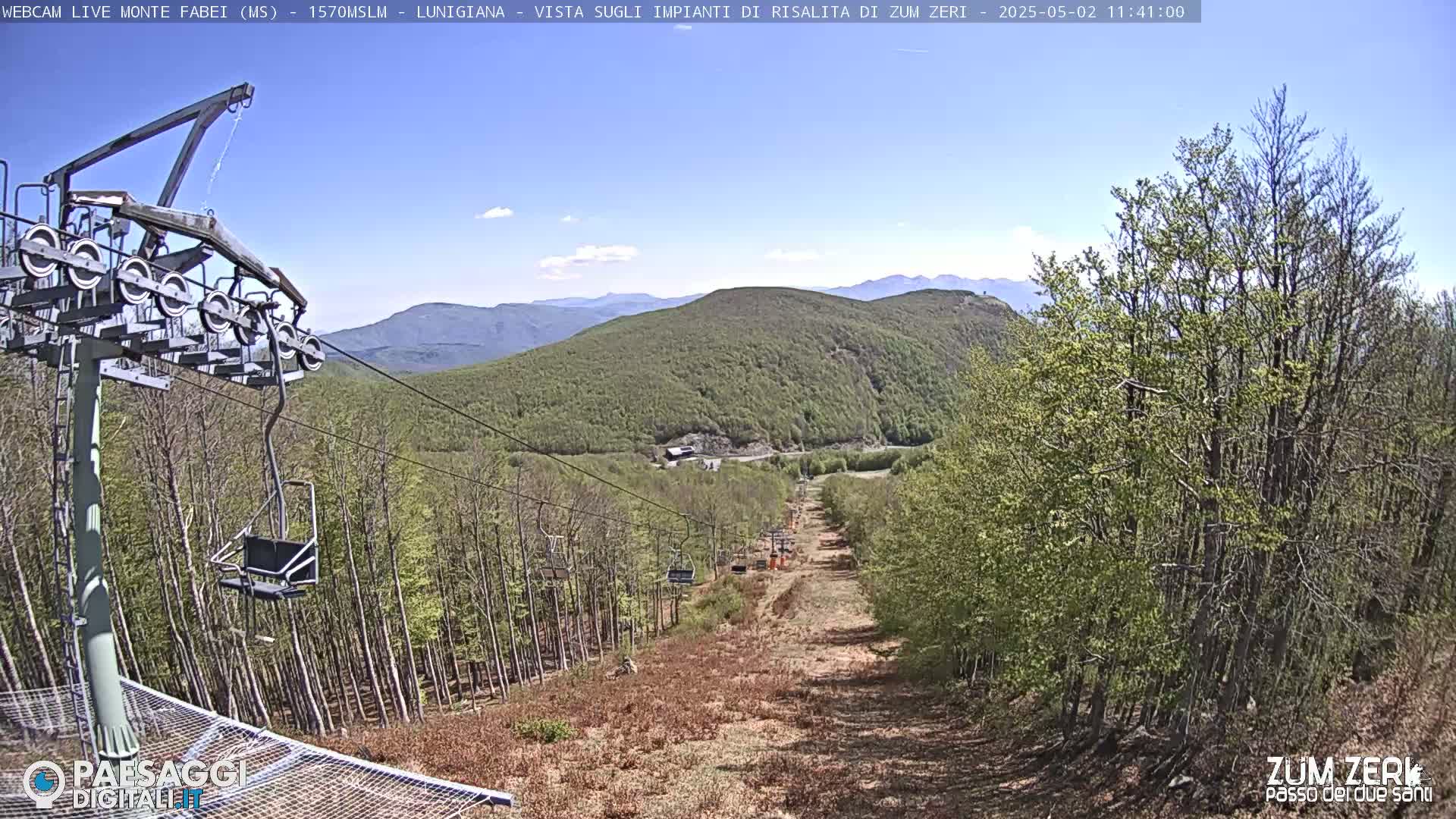 A chairlift ascends a mountainside covered in a mix of bare and budding trees under a clear blue sky.