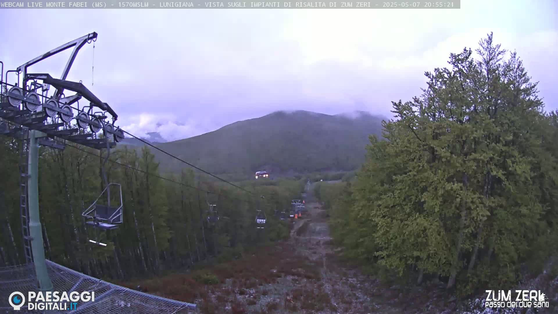 A chairlift rises through a misty, forested mountain landscape.