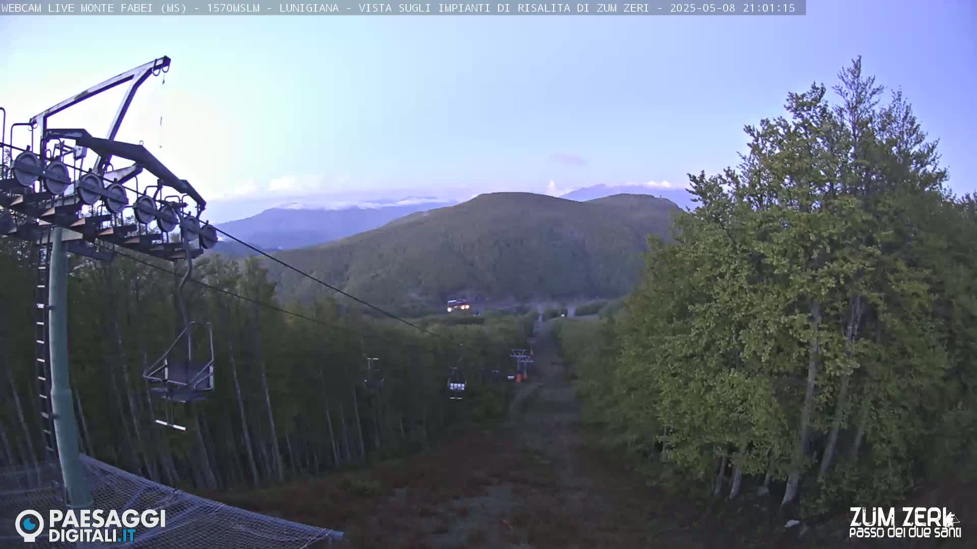 A chairlift ascends a mountainside at dusk, overlooking a forest under a clear sky.