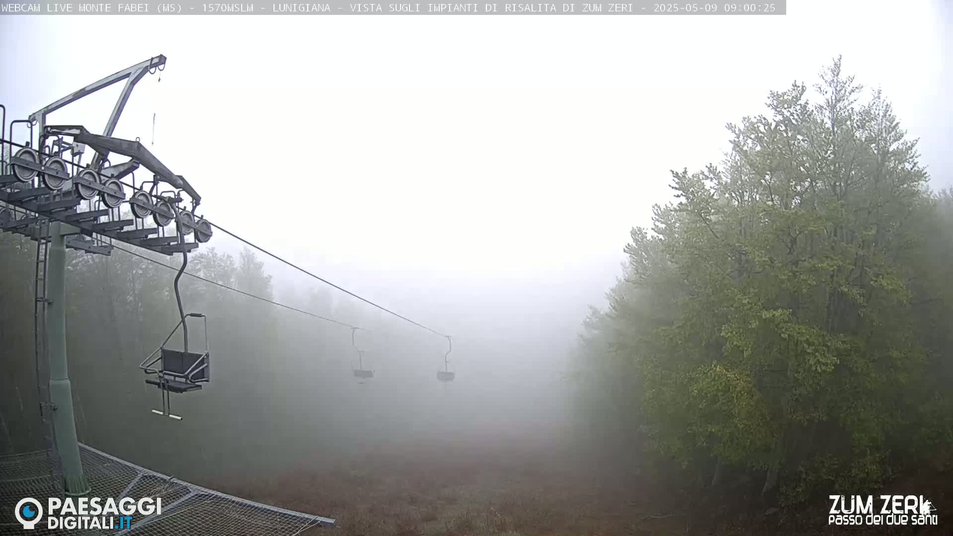 A foggy mountain landscape features a chairlift with empty chairs and trees shrouded in mist.