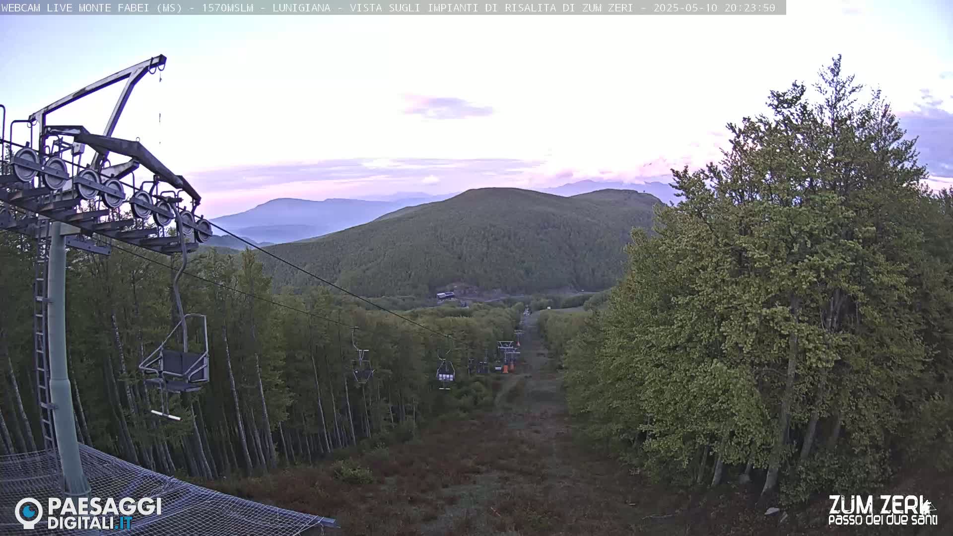 A chairlift ascends a mountainside at dusk, overlooking a forest bathed in the soft light of twilight.