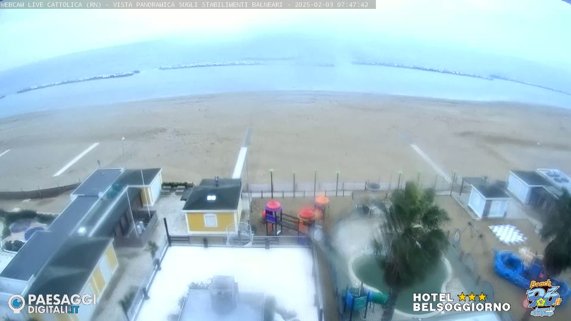 A beach with buildings and a playground is seen from above on an overcast day.