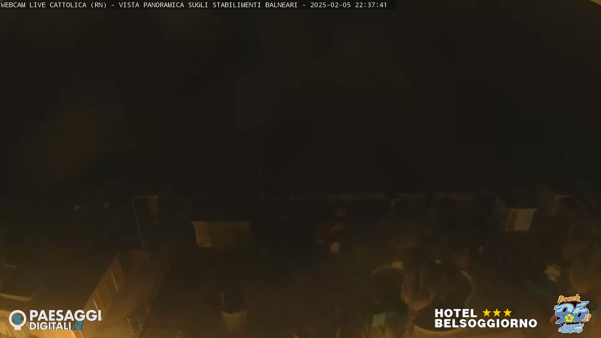A dark, nighttime view of a mostly obscured outdoor area, possibly a patio or beach, with a few indistinct figures present.
