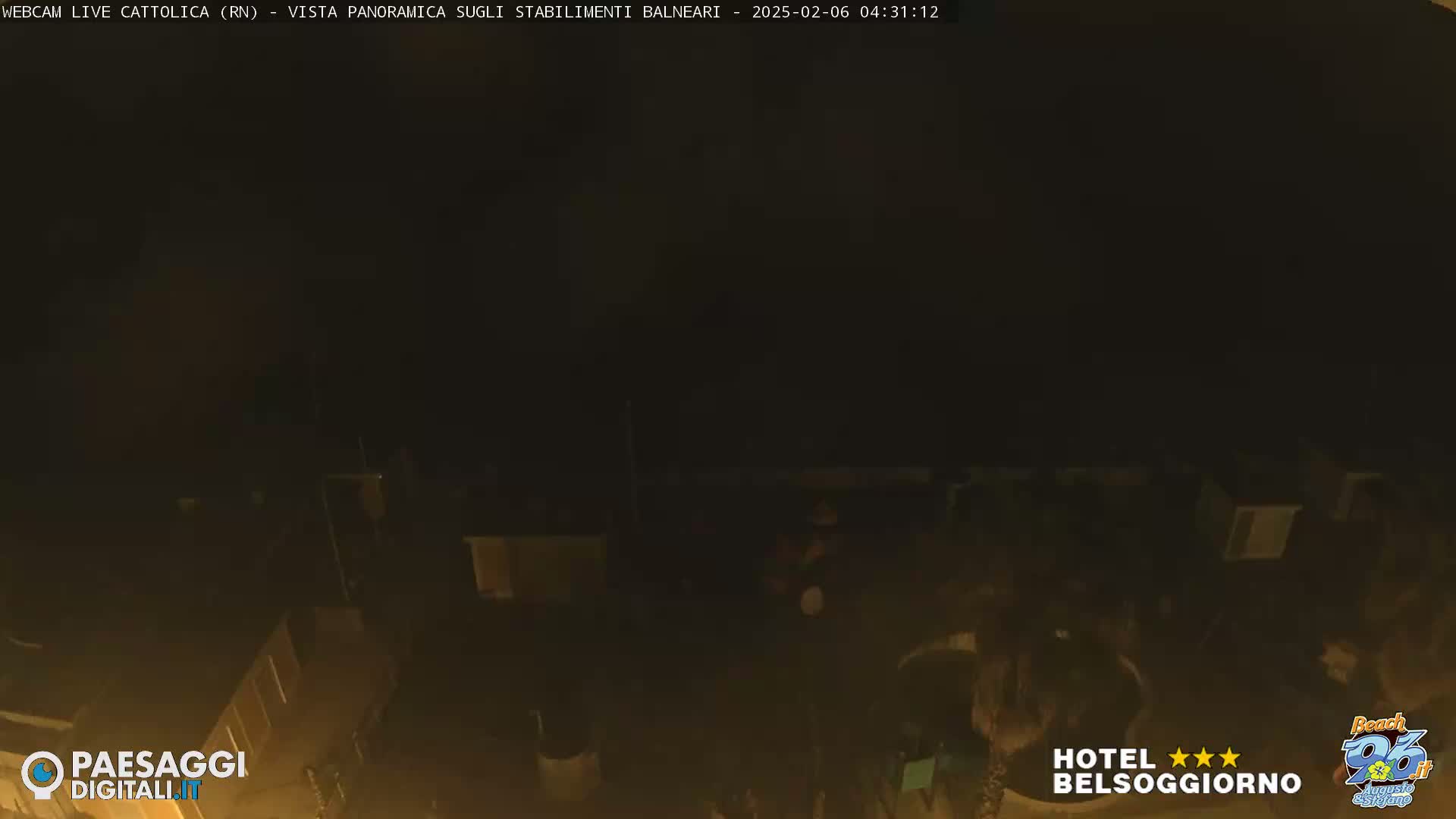A nighttime, low-light view of a beach area with structures, possibly beach huts, and some people visible.