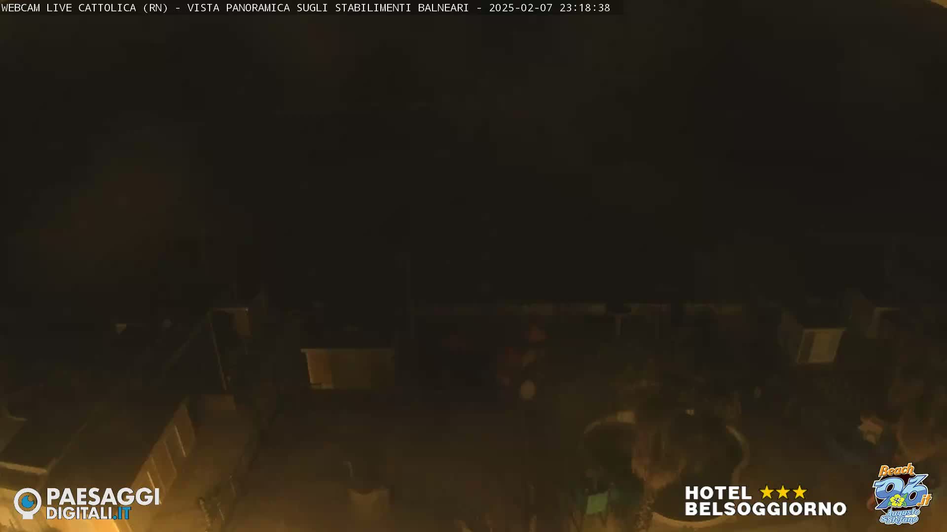 A nighttime, low-light view of a beachside area with several structures and some people visible.