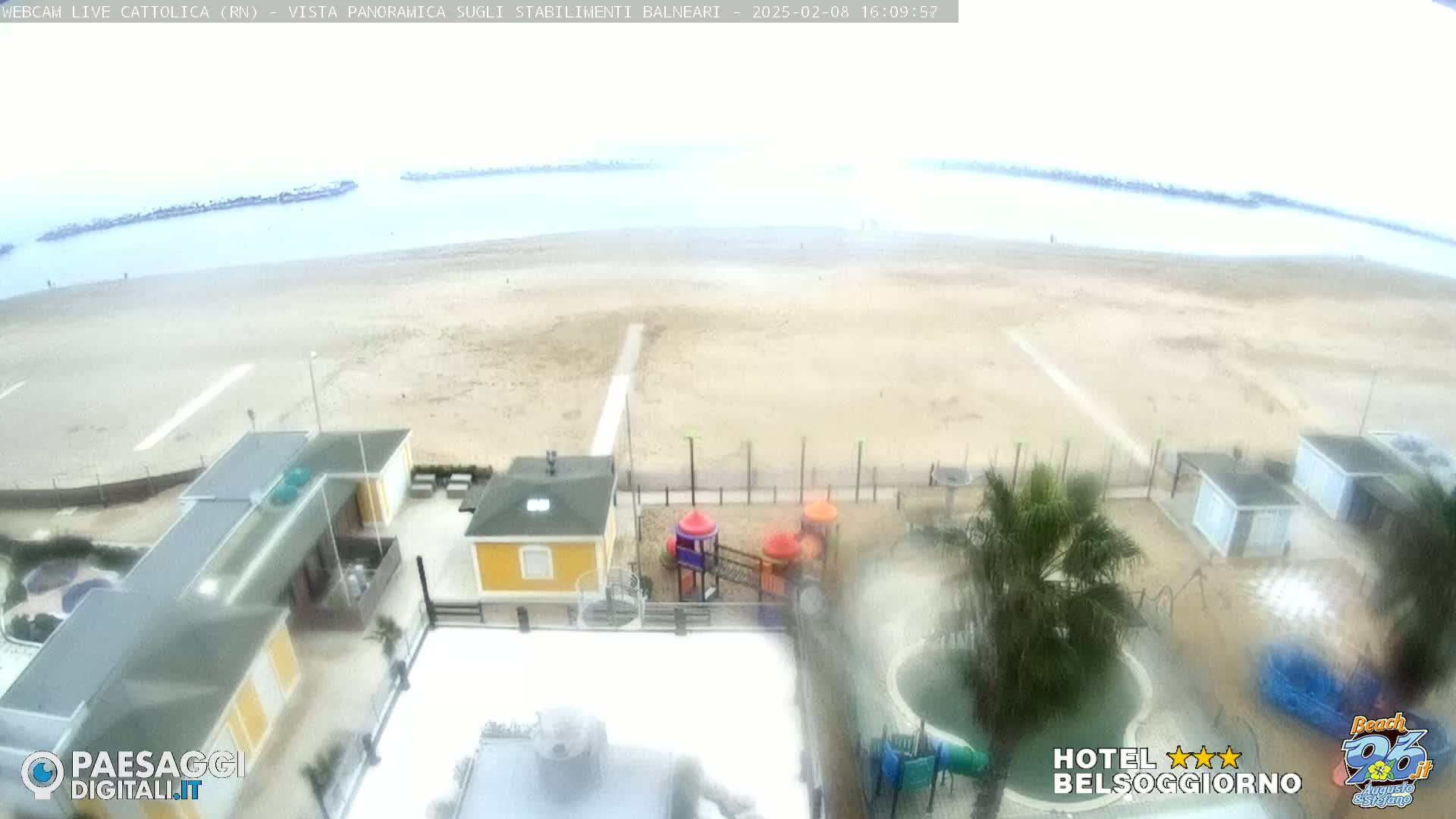 A hazy view of a beach and seaside buildings with a playground, under overcast skies.