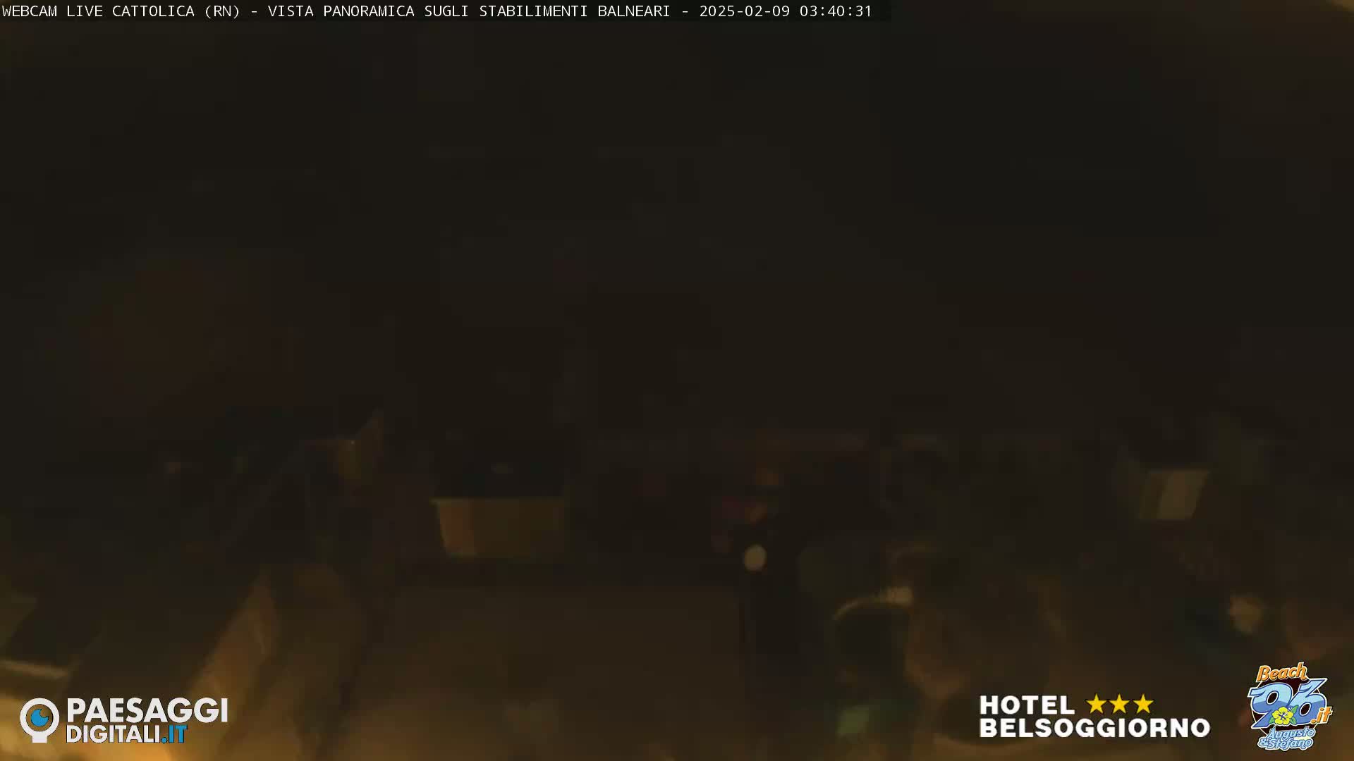 A dark, nighttime view of a beach area with indistinct shapes suggesting people and structures.