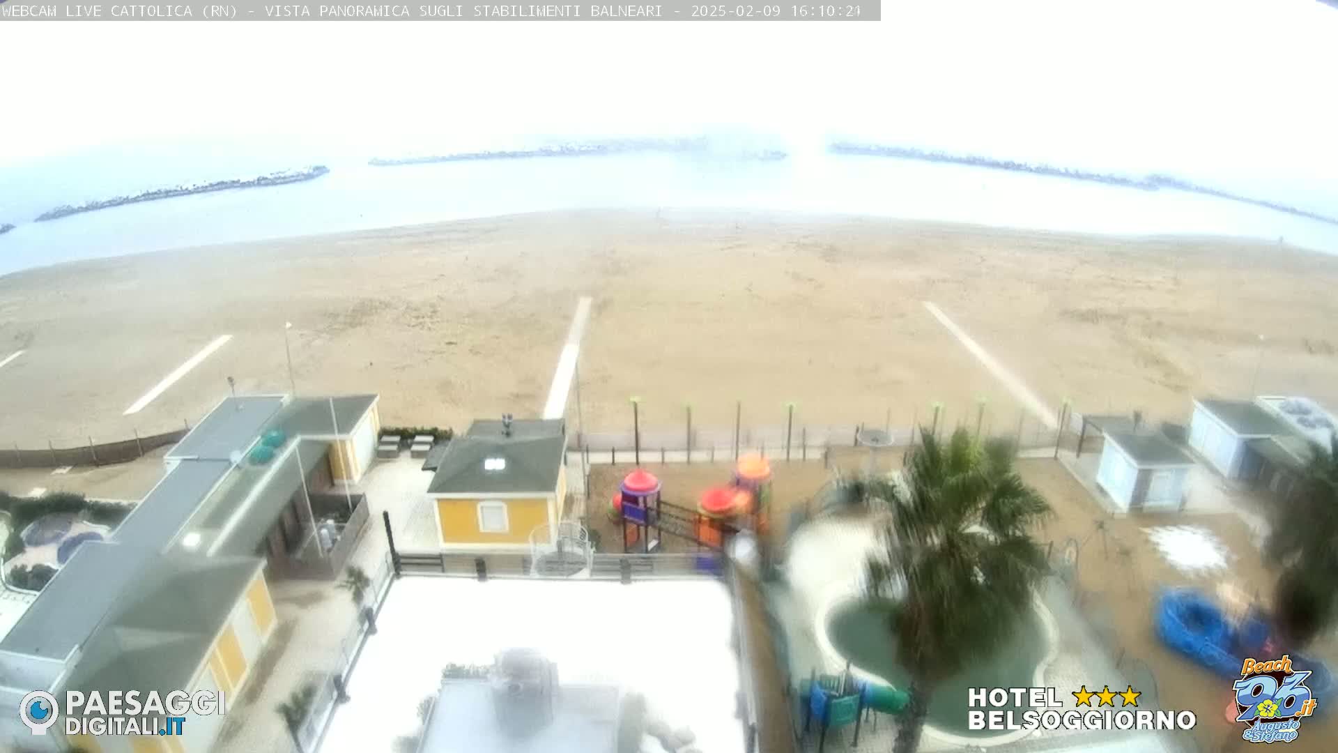 A beach with a few buildings and a playground is visible under an overcast sky.