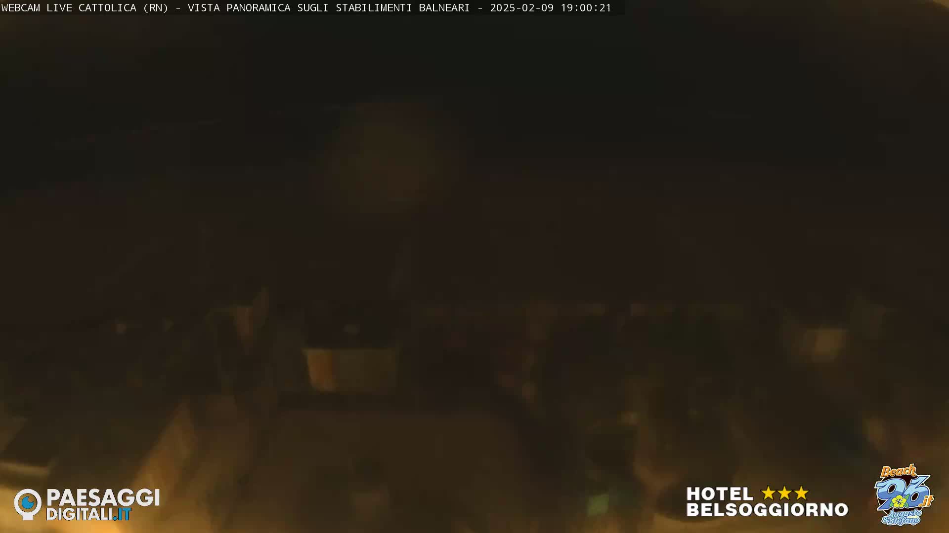A dark, nighttime scene shows a blurry collection of people gathered in an outdoor area.