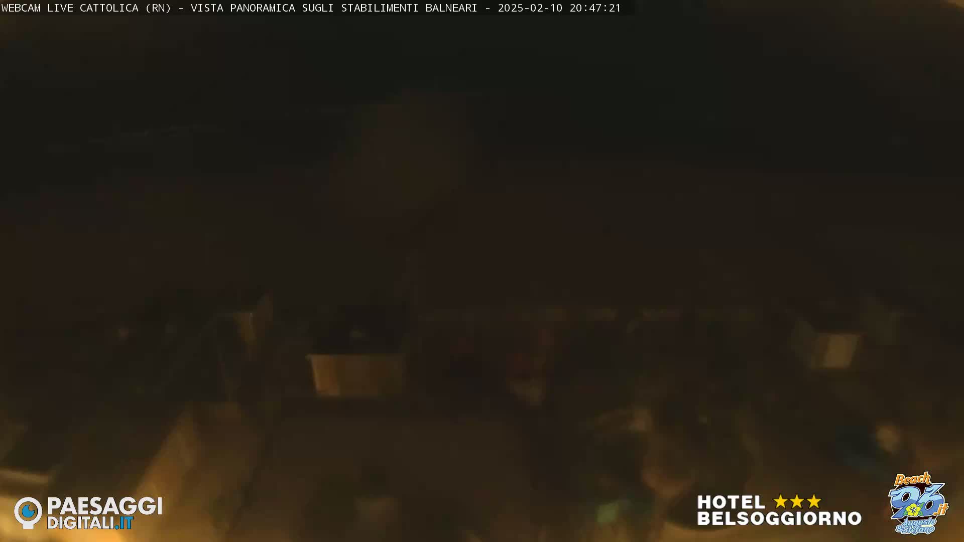 A dark, nighttime scene shows a blurry view of a beach area with indistinct shapes suggesting people and structures.
