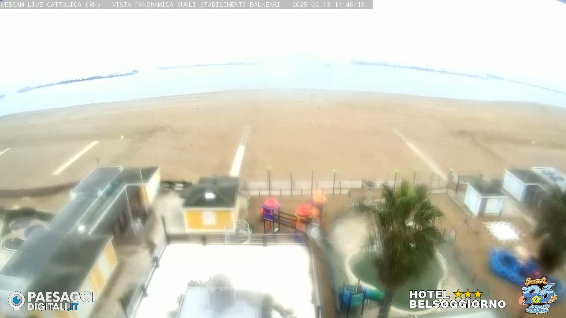 An overcast day reveals a beach with buildings and a playground near the water.