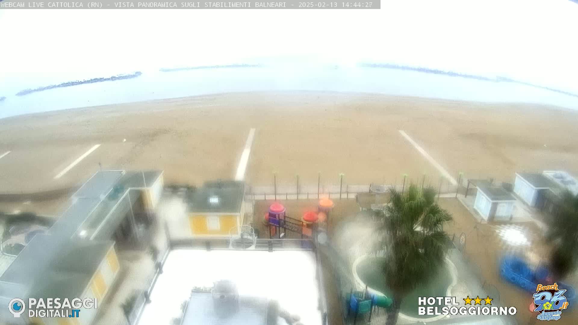 A beach with a playground and some buildings is seen from an elevated viewpoint on an overcast day.