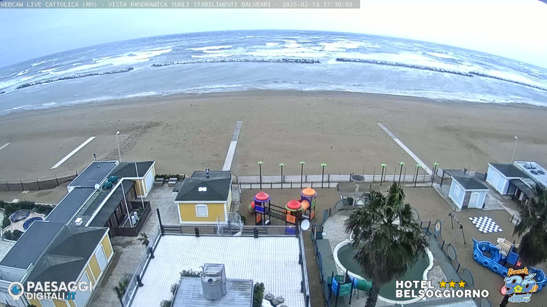 A beach scene shows choppy waves under an overcast sky, with a sandy beach, beachside buildings, a playground, and a swimming pool.