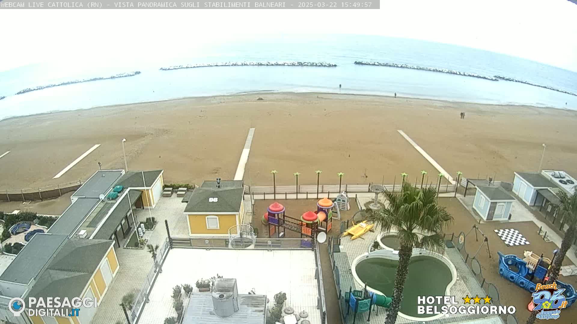 An overcast day at a beach with sand-colored sand, several beach buildings, a playground, and swimming pools.
