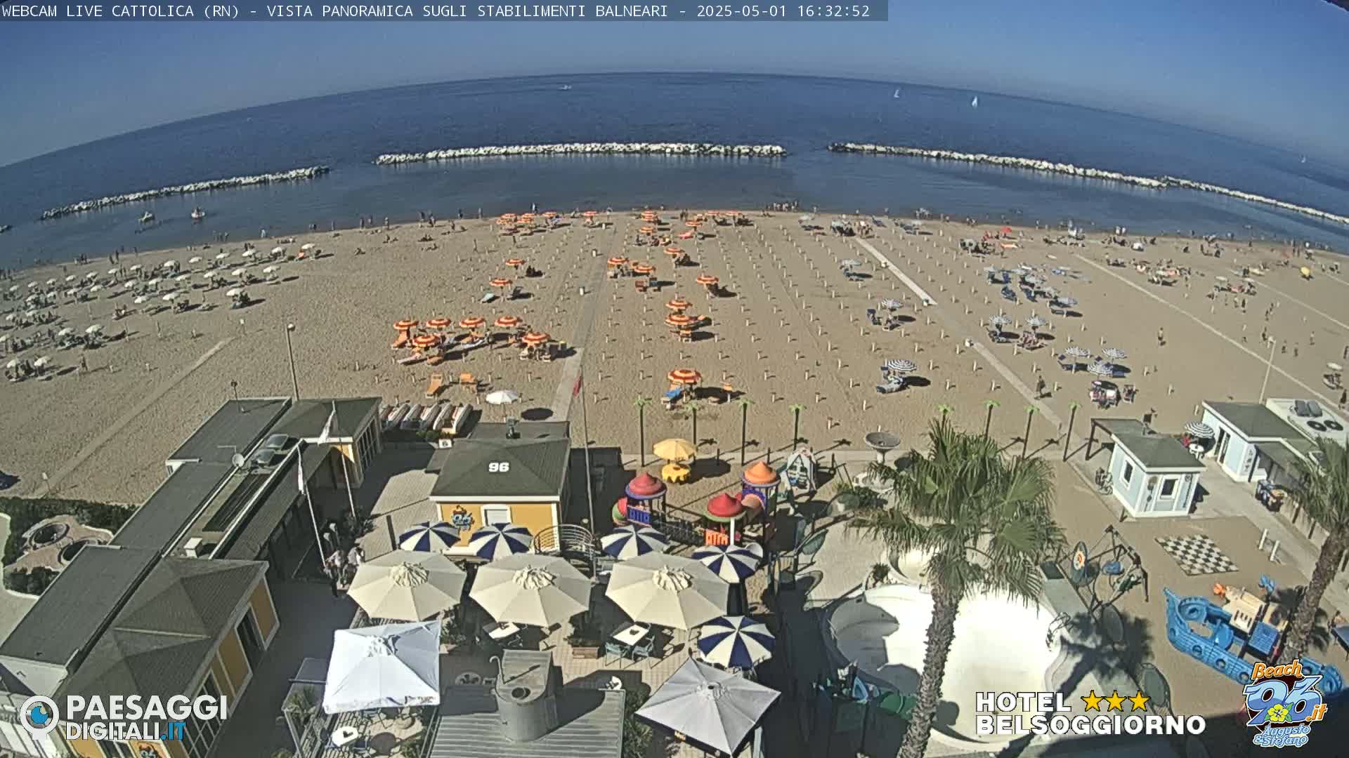 A sandy beach with numerous umbrellas and beachgoers is shown, alongside beachside buildings and a children's playground, all under sunny skies.