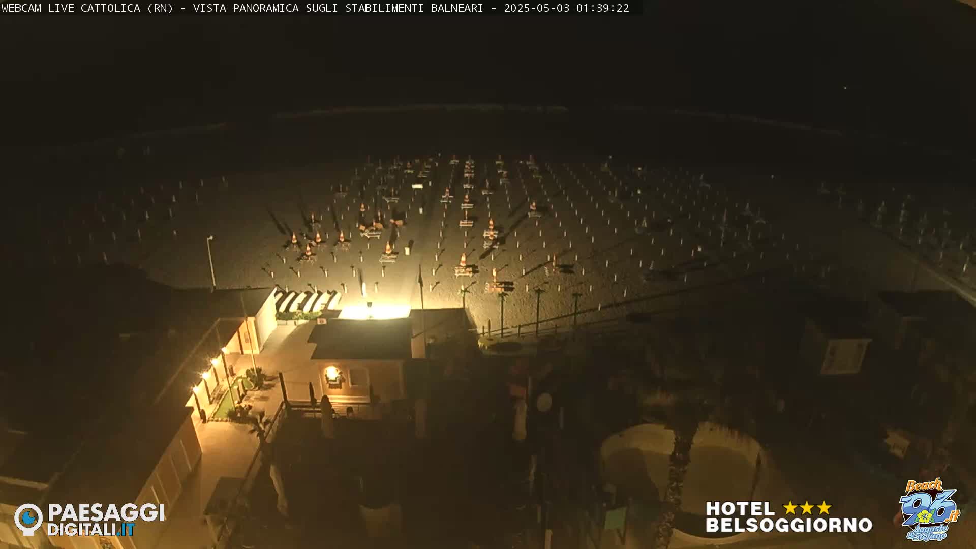 A dark, nighttime view of a beach with numerous empty beach umbrellas and tables arranged in rows.