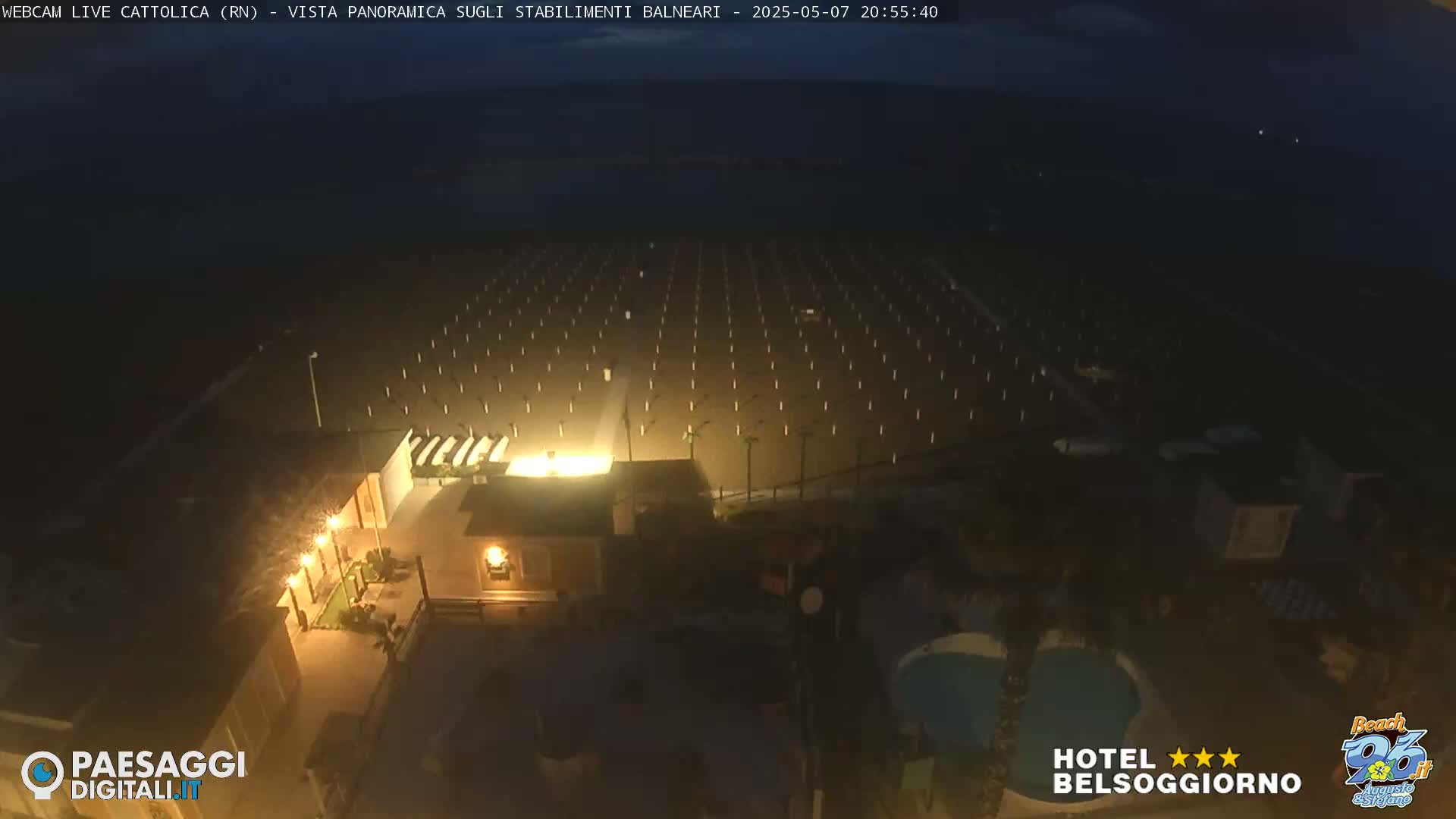 A nighttime, aerial view of a beach at night showing rows of beach umbrellas and a building with a pool.