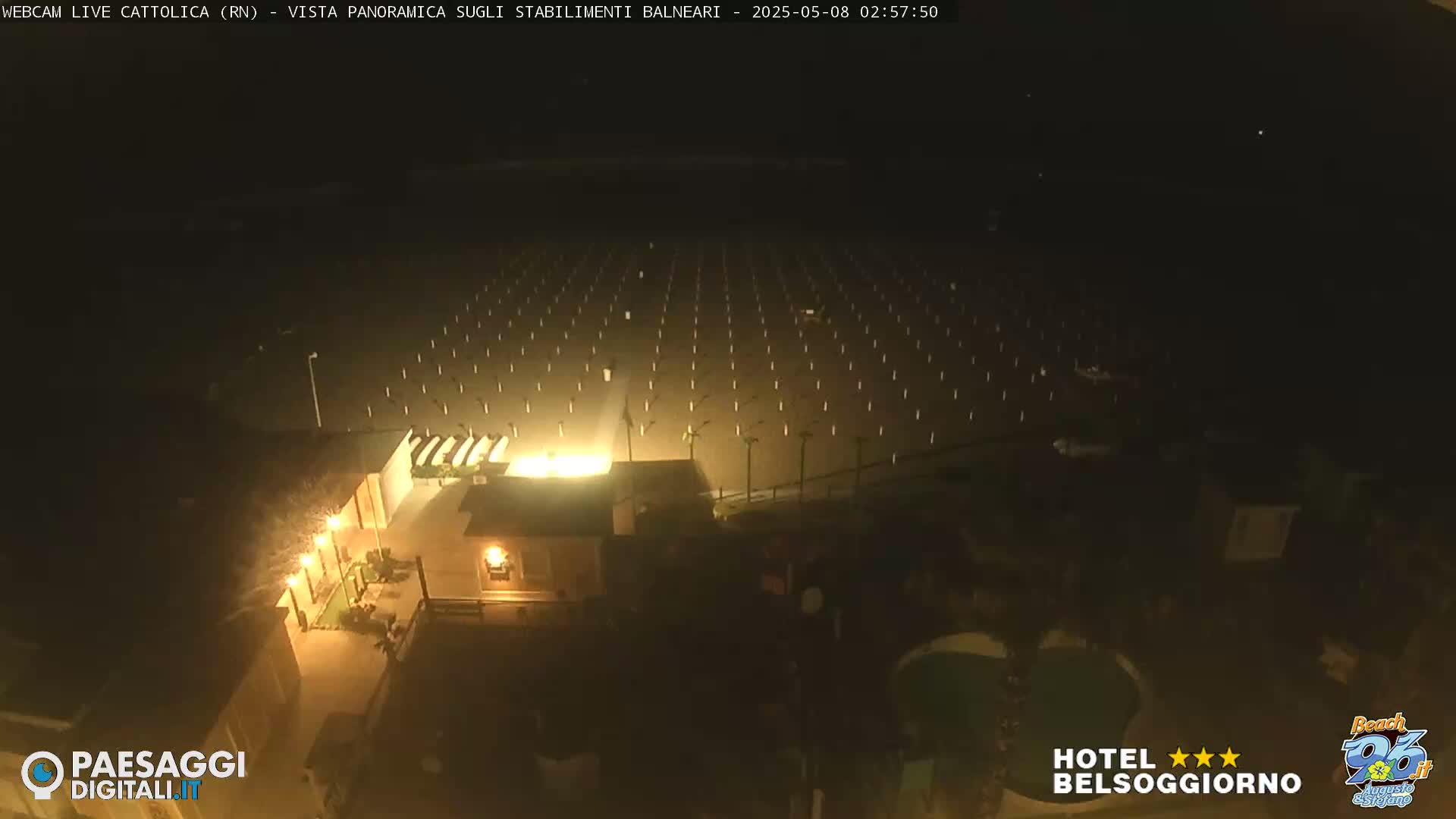 A nighttime, high-angle view shows a beach with evenly spaced posts illuminated under a dark sky.