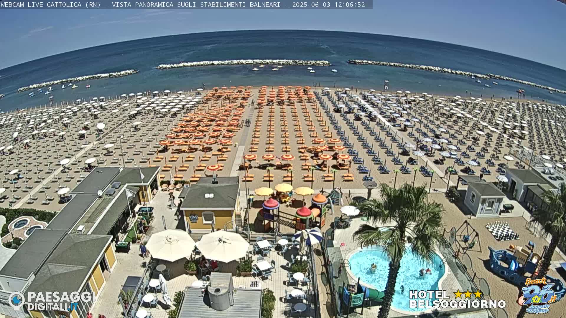 A crowded beach with numerous orange and white umbrellas, lounge chairs, and beach-side amenities under a clear blue sky.