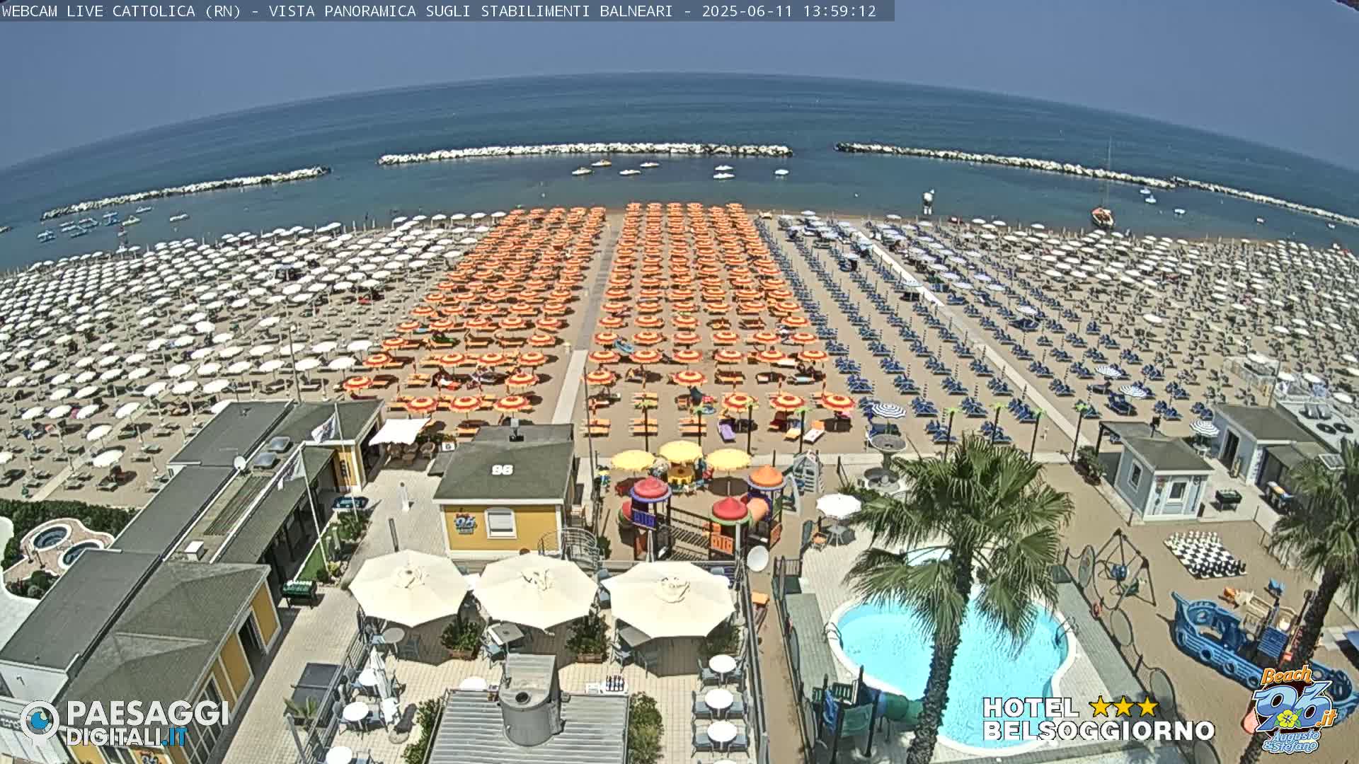 A beach with hundreds of orange and white umbrellas, beach chairs, and a playground is shown under a clear blue sky.